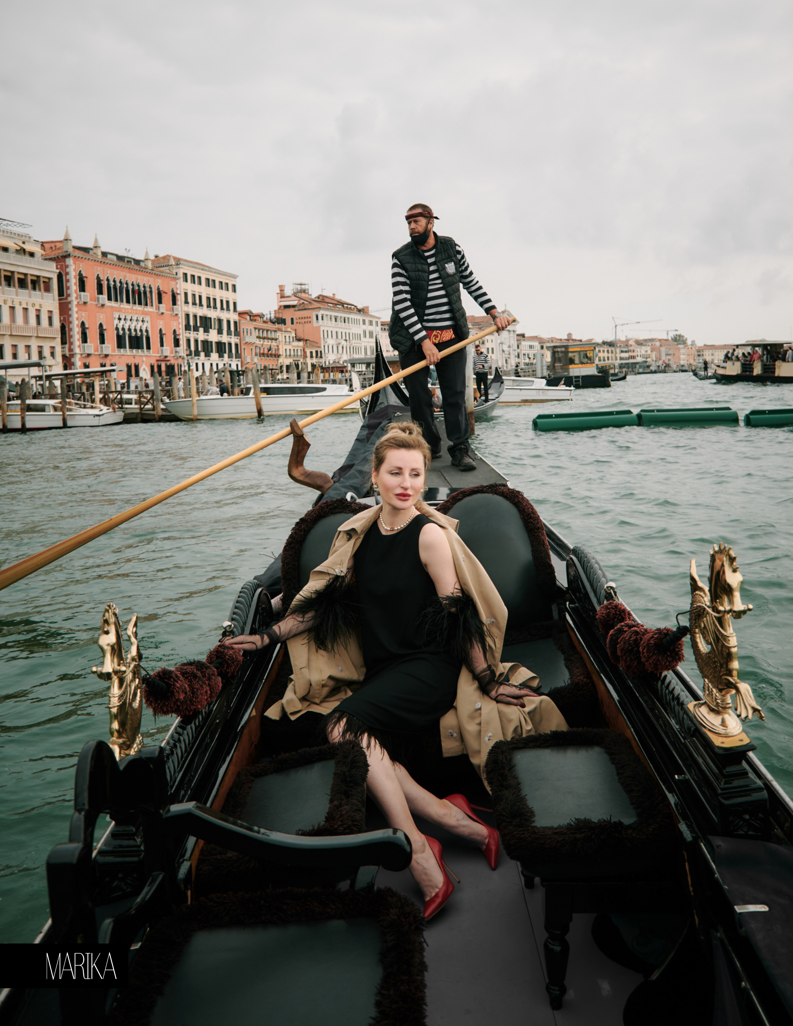 A mesmerizing young woman in a black dress sits on a gondola, gliding through the narrow streets of Venice. The black and white striped shirt of the gondolier is visible in the background. The woman's silky hair flows in the breeze, and her captivating eyes gaze off into the distance. The winding streets of Venice create a beautiful, romantic backdrop for this enchanting photo.