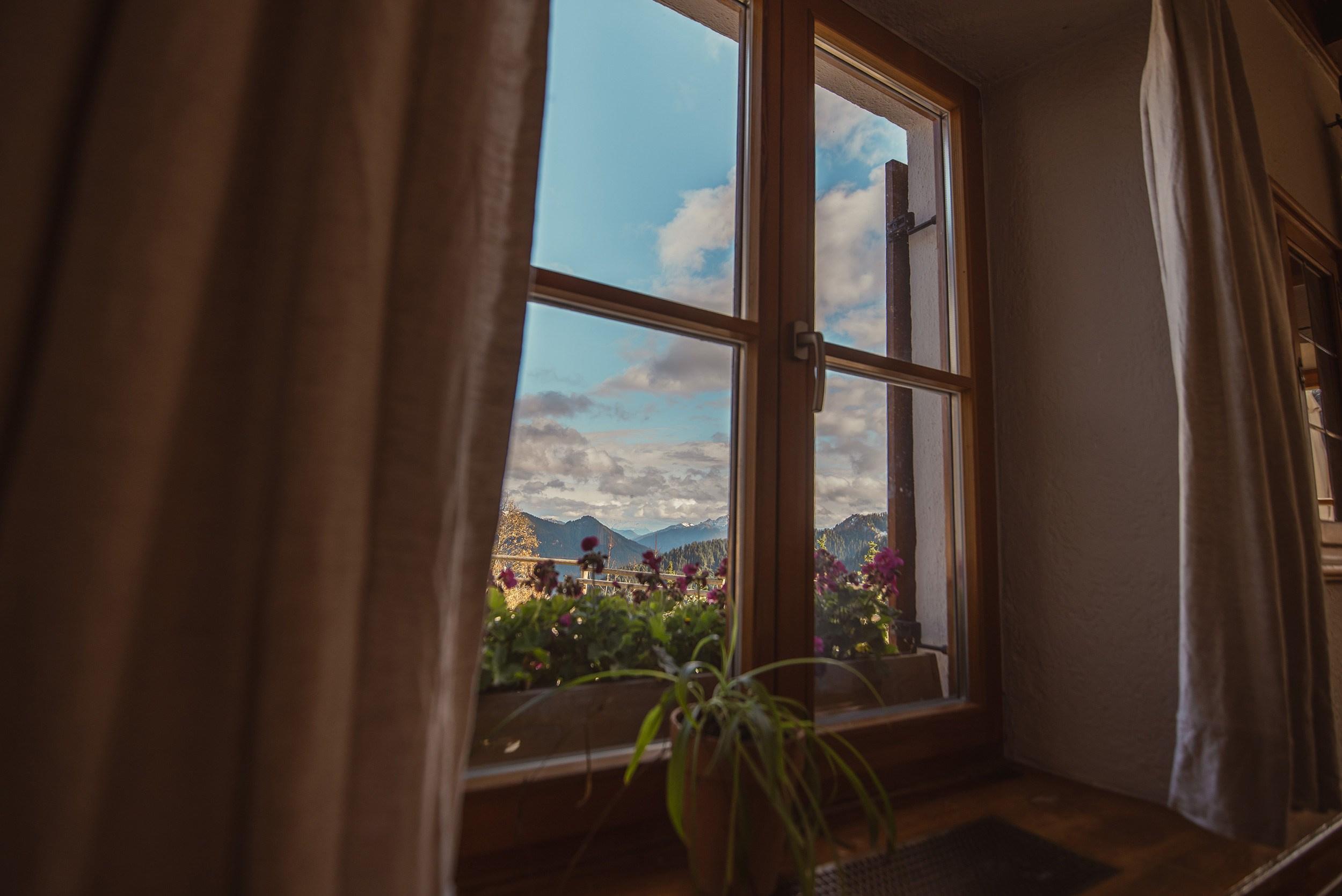 View through a window at Alte Wallberghaus alpine hotel overlooking the pine forest and Lake Tegernsee.