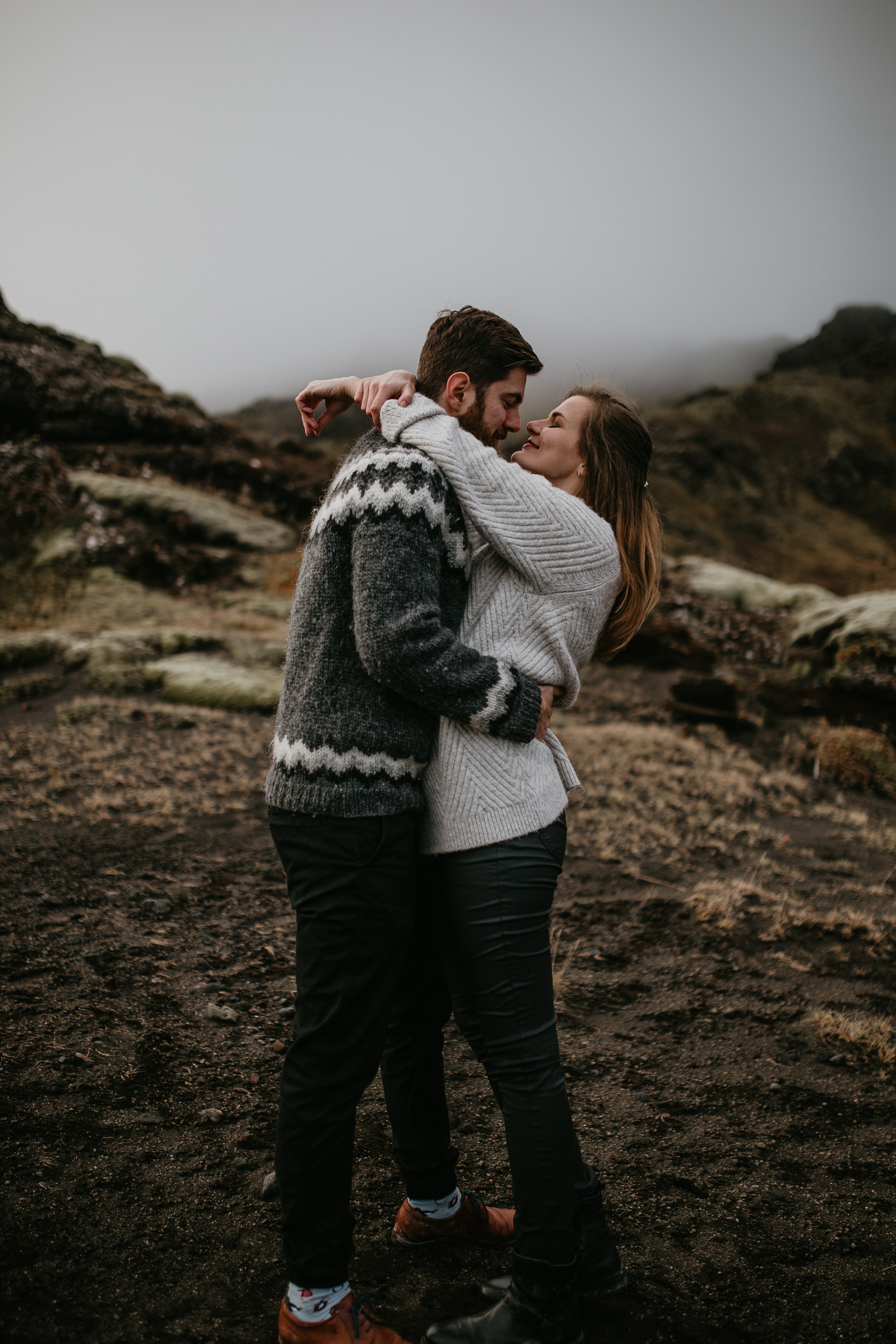 Adventurous couple standing on a black sand beach in Iceland, with dramatic cliffs in the background.