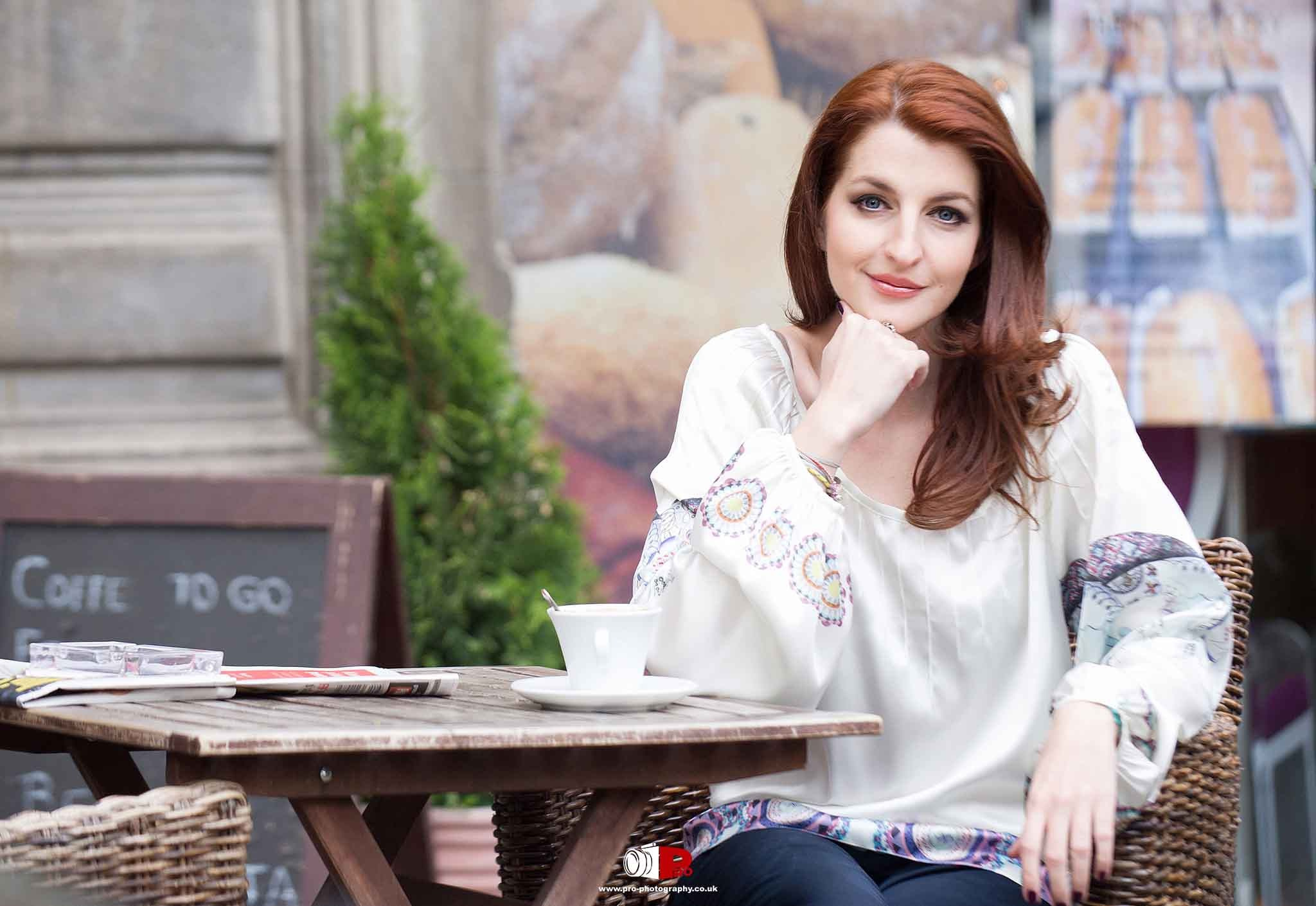 A smiling woman enjoys coffee at an outdoor café, seated in a warm and inviting setting.