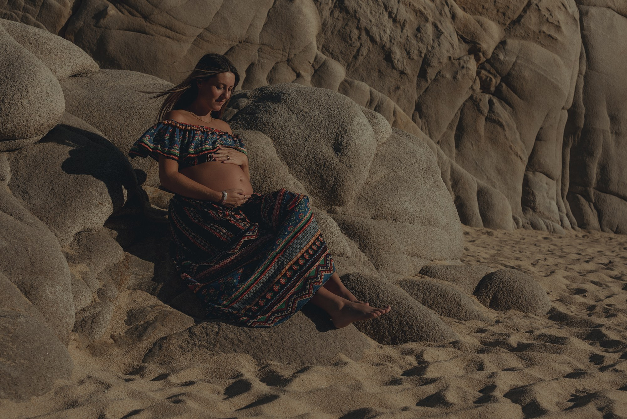 Los Cabos maternity photography – expecting couple and mother-to-be captured at Playa del Amor with cinematic style, warm color grading, ocean and rocky cliffs in the background