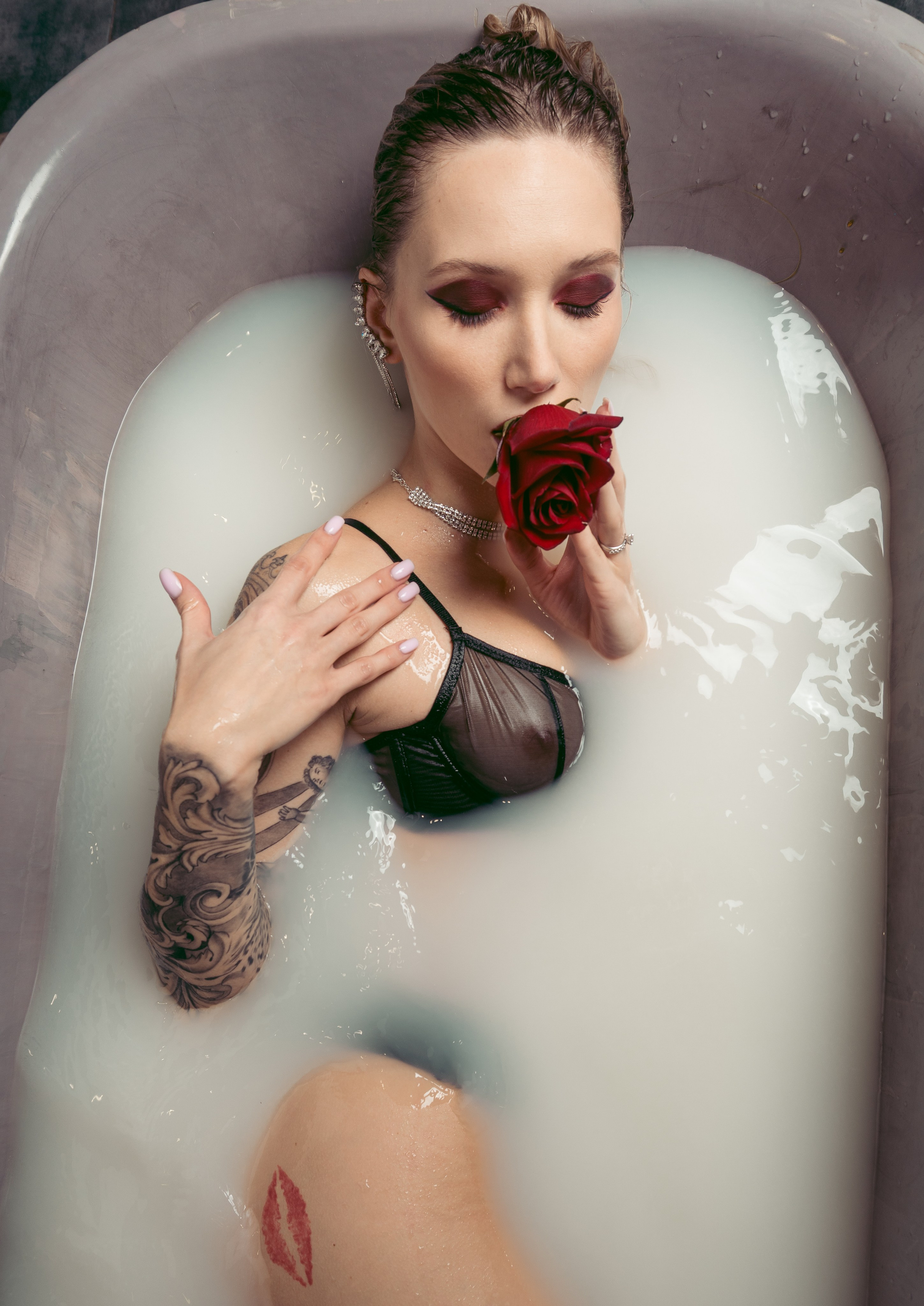 Top view of a woman in a bath with white water, holding a rose.