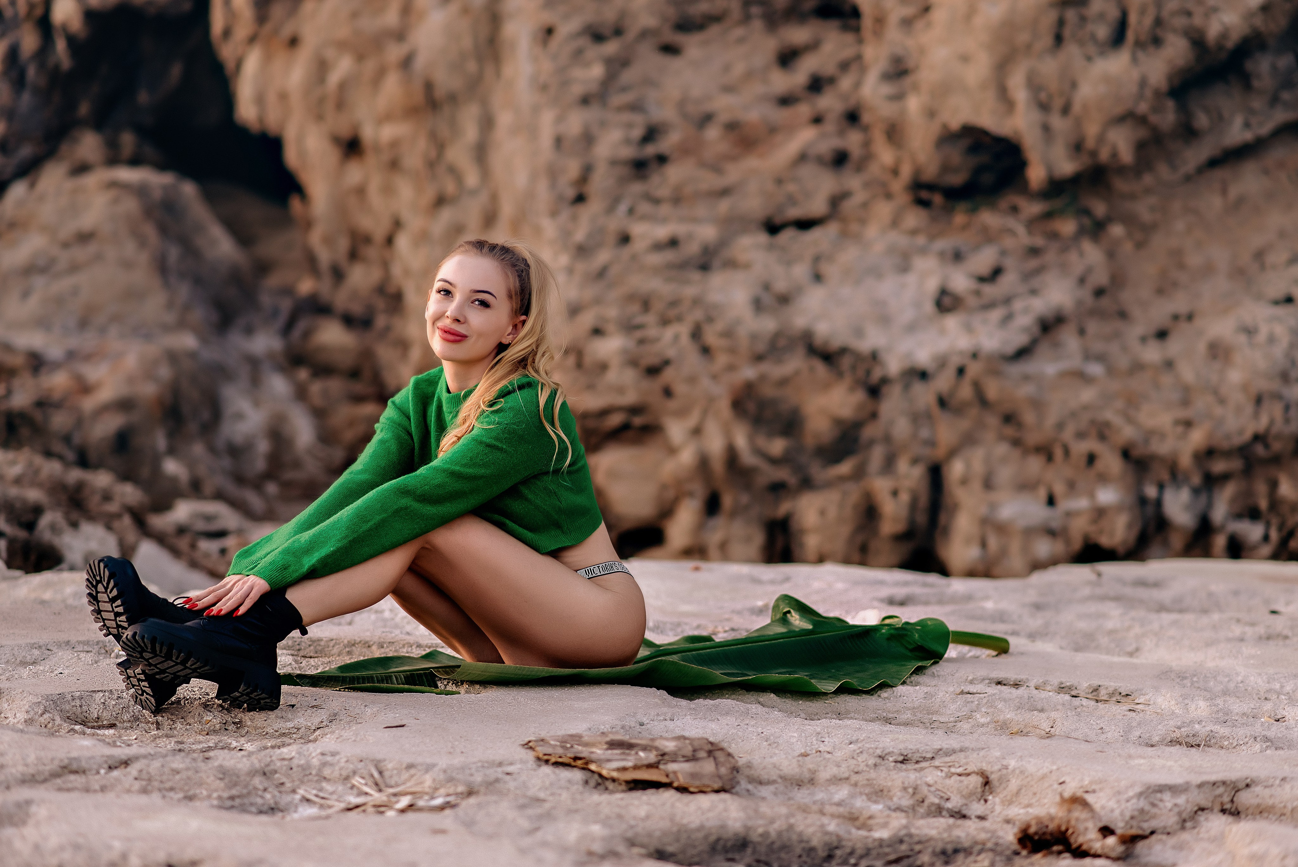Девушка в зеленом свитере и ботинках на фоне скал.