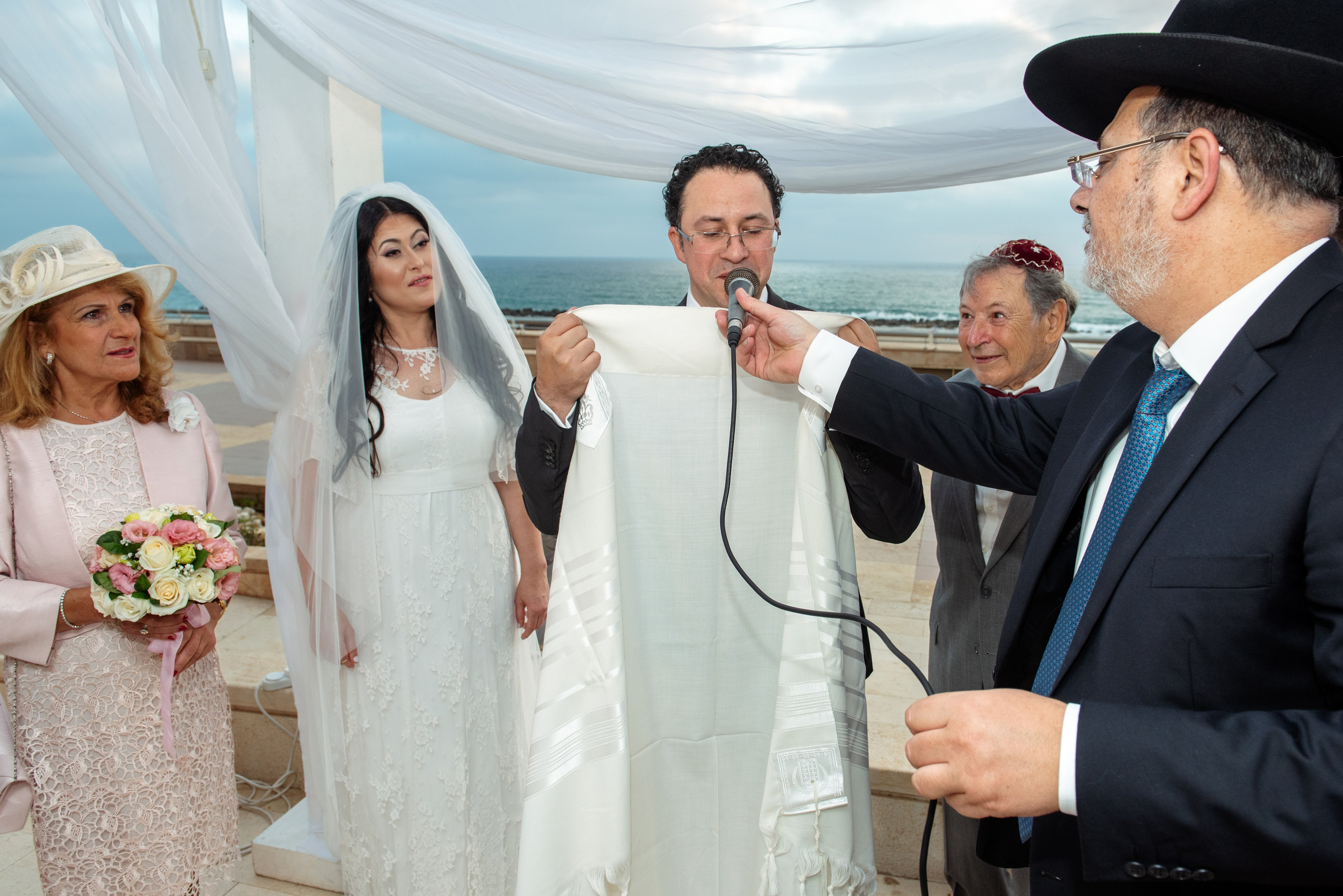 Bride and groom standing under the chuppah at the Leonardo Hotel in Haifa, surrounded by emotion.