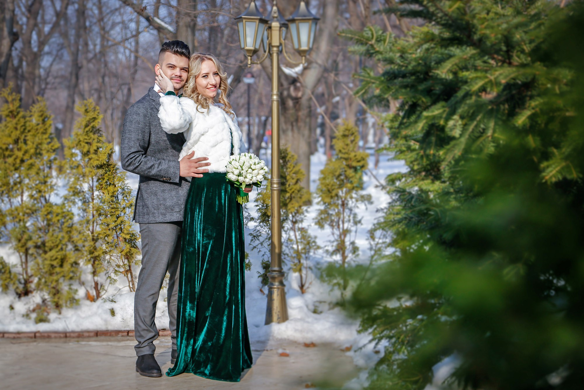 The groom looking lovingly at his bride while keeping her warm, a touching and cozy moment captured in the white winter scenery.