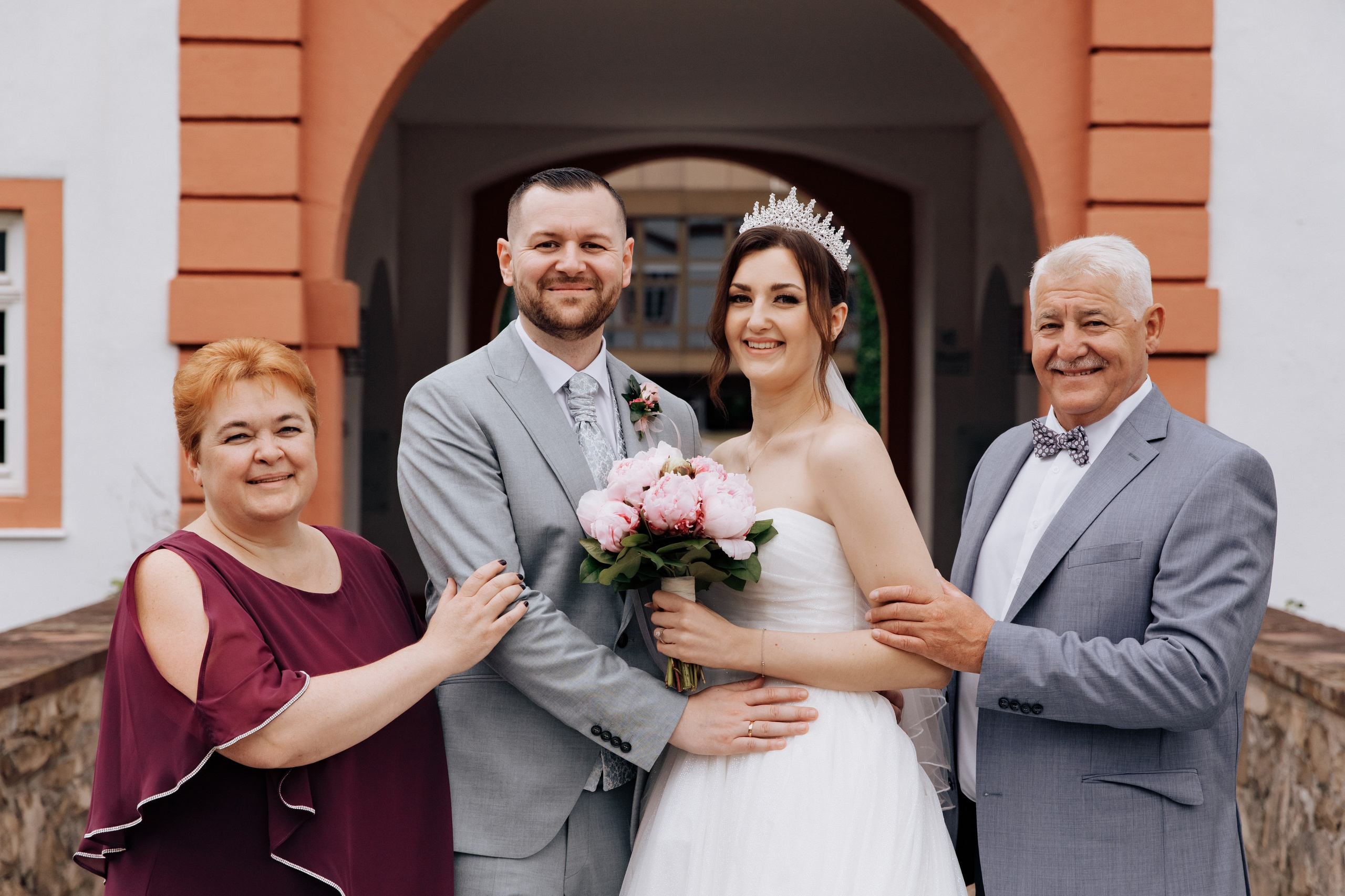 Porträt der Braut und dem Bräutigam sowie den Eltern der Braut. Alle lächeln glücklich in die Kamera.