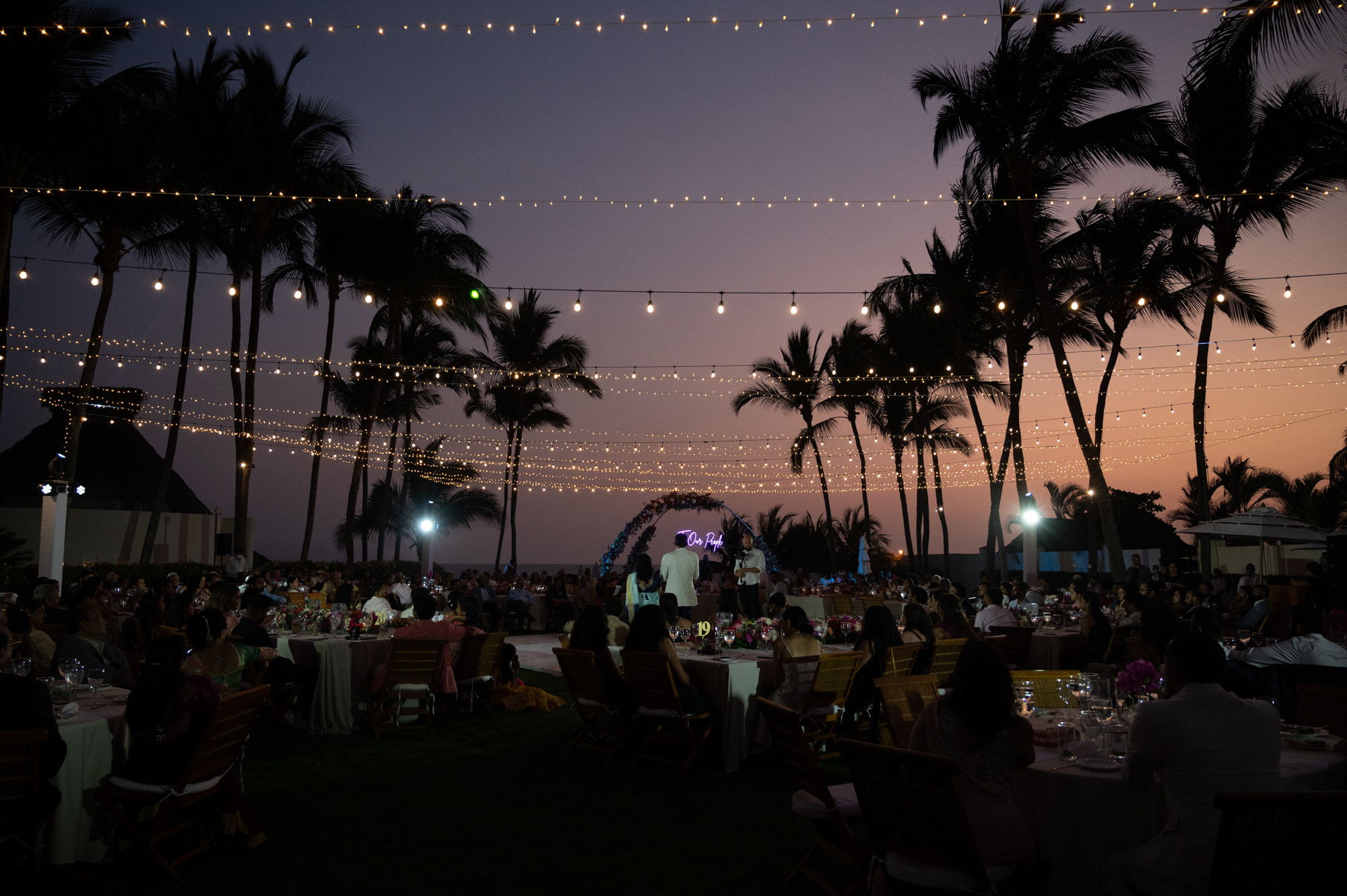 a group of people sitting at tables under string lights