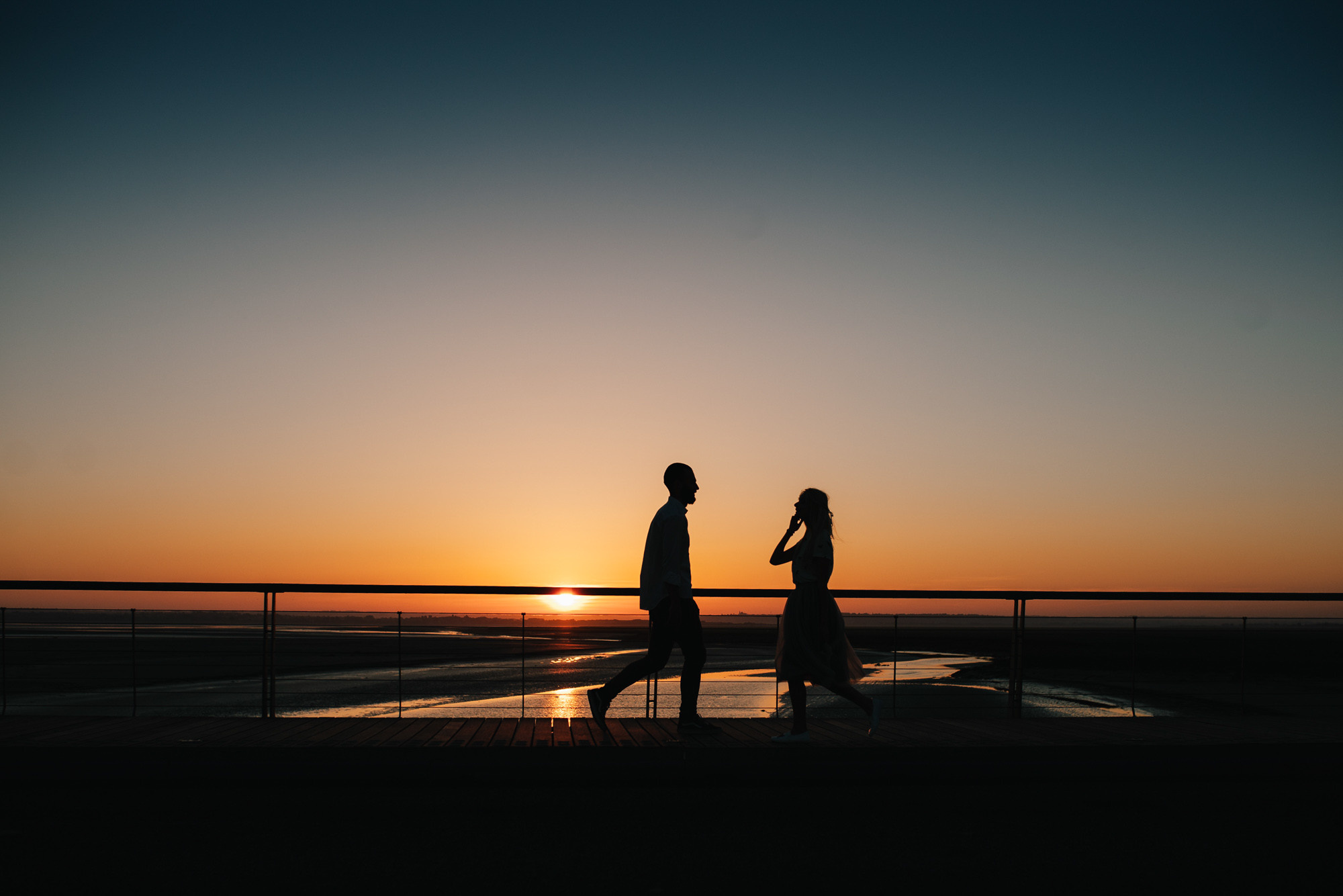 a couple standing on a bridge at sunset