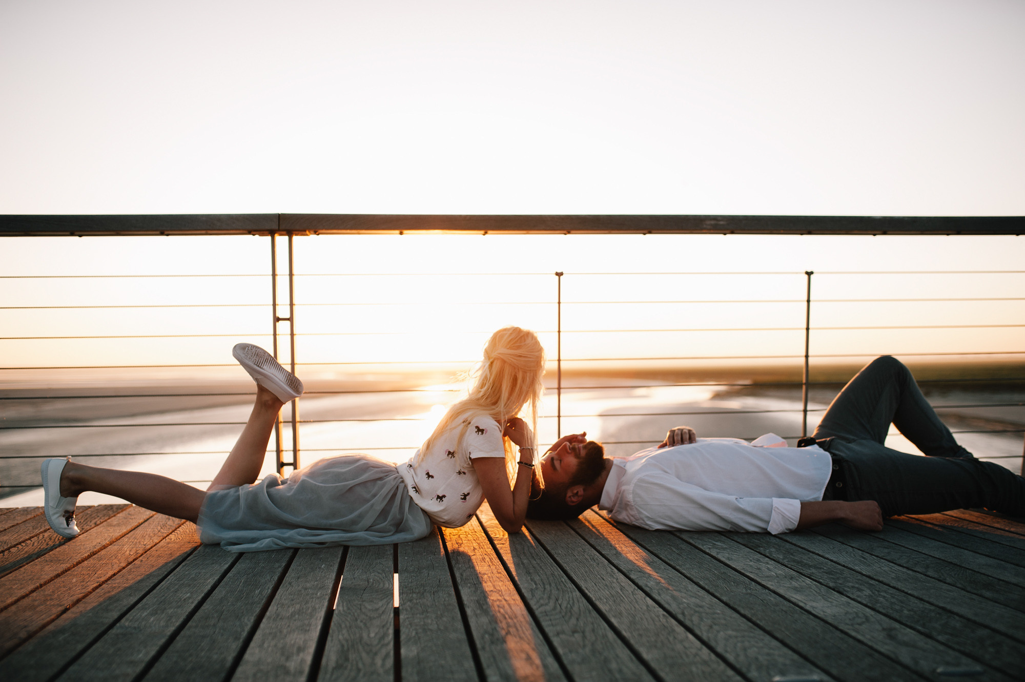 a couple laying on a wooden deck at sunset