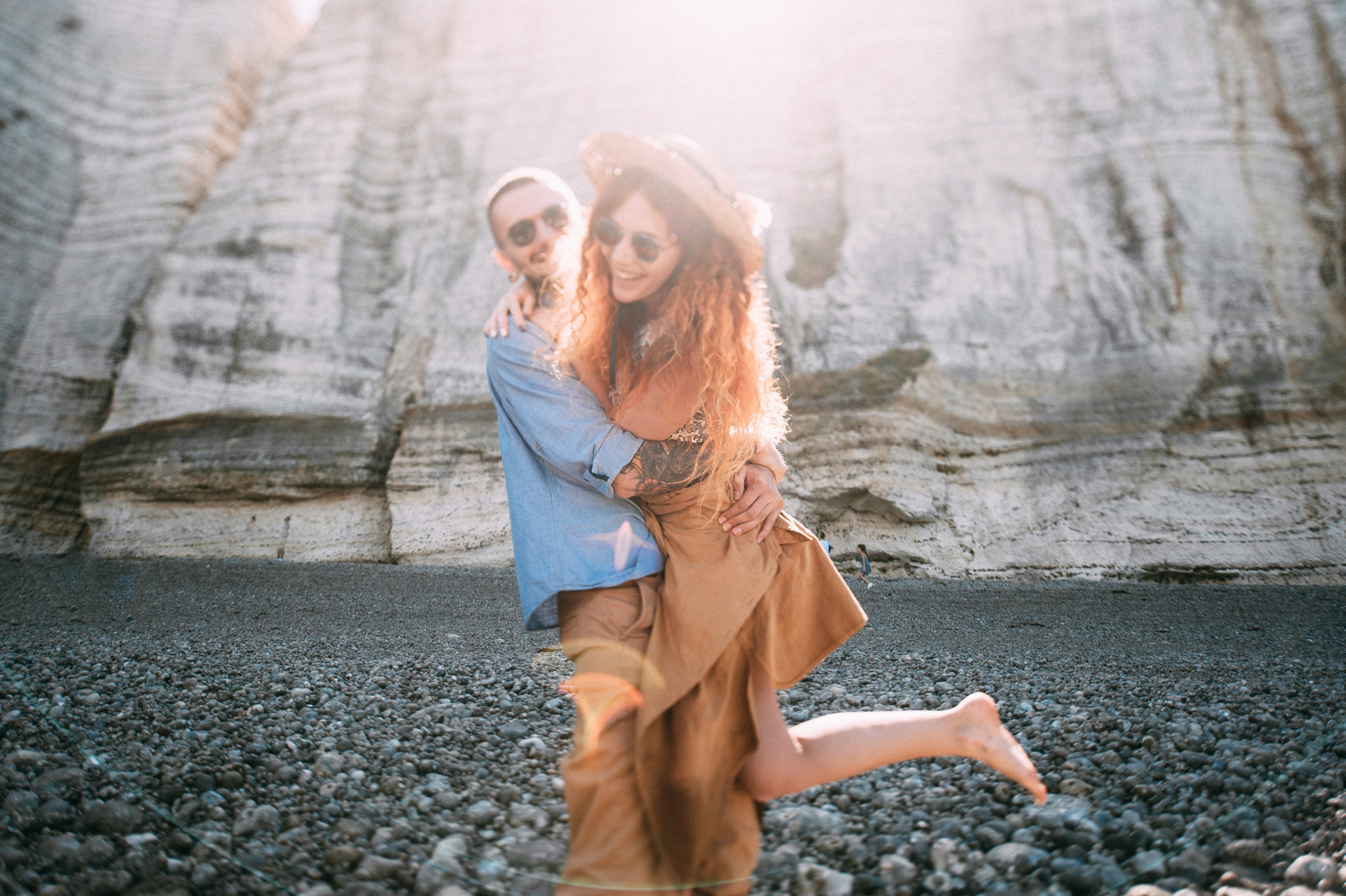 a woman in a blue shirt and tan pants is dancing on a rocky beach