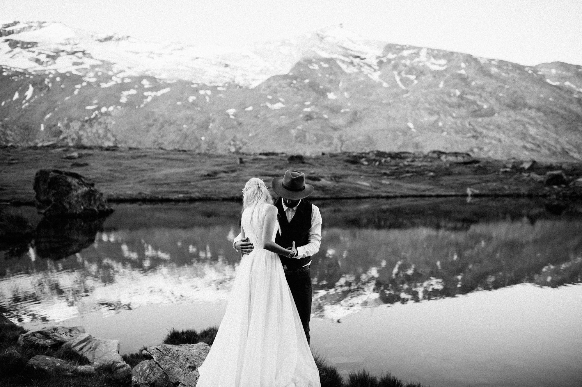 a bride and groom standing by a lake in the mountains