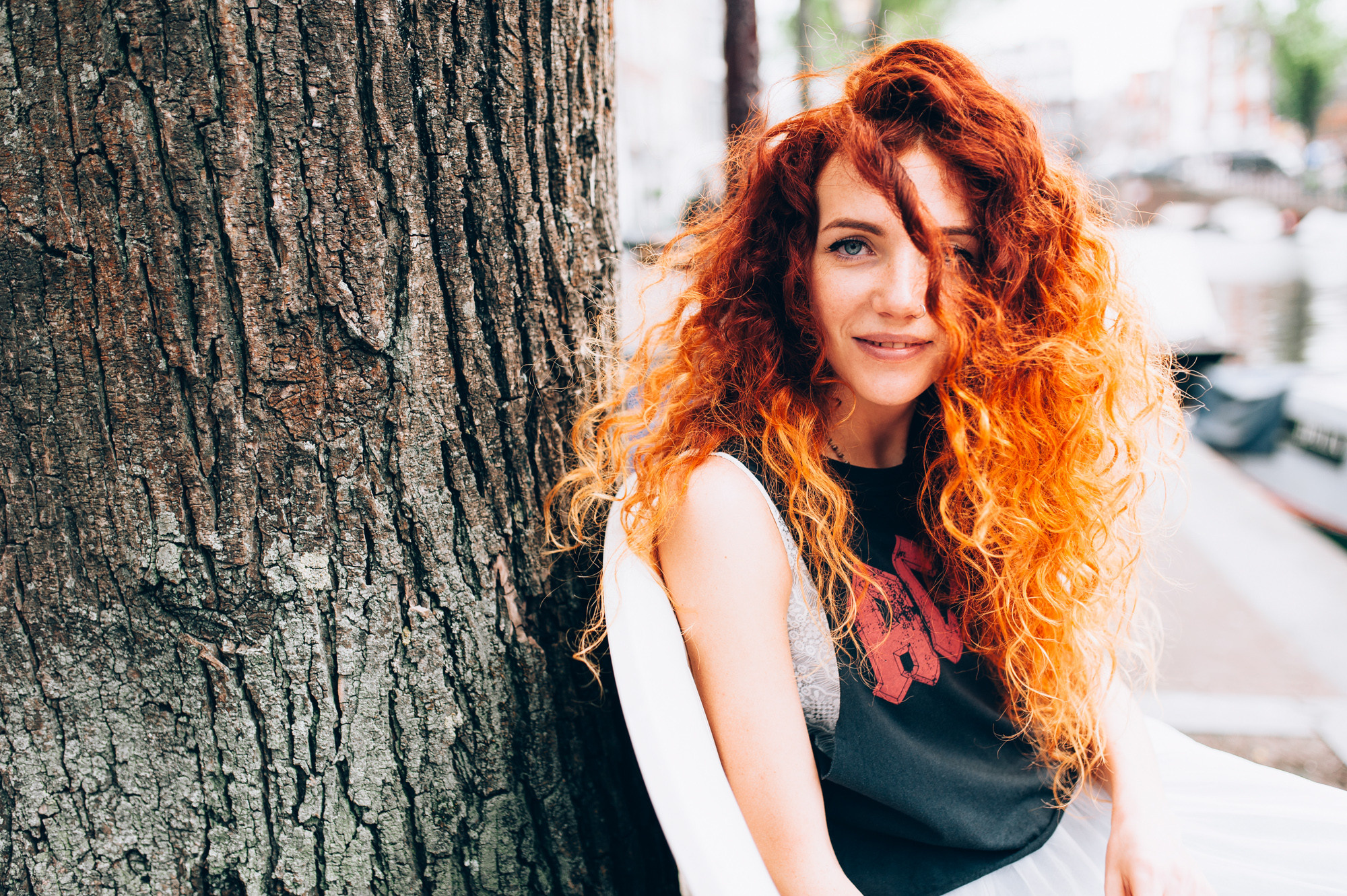 a woman with red hair sitting next to a tree