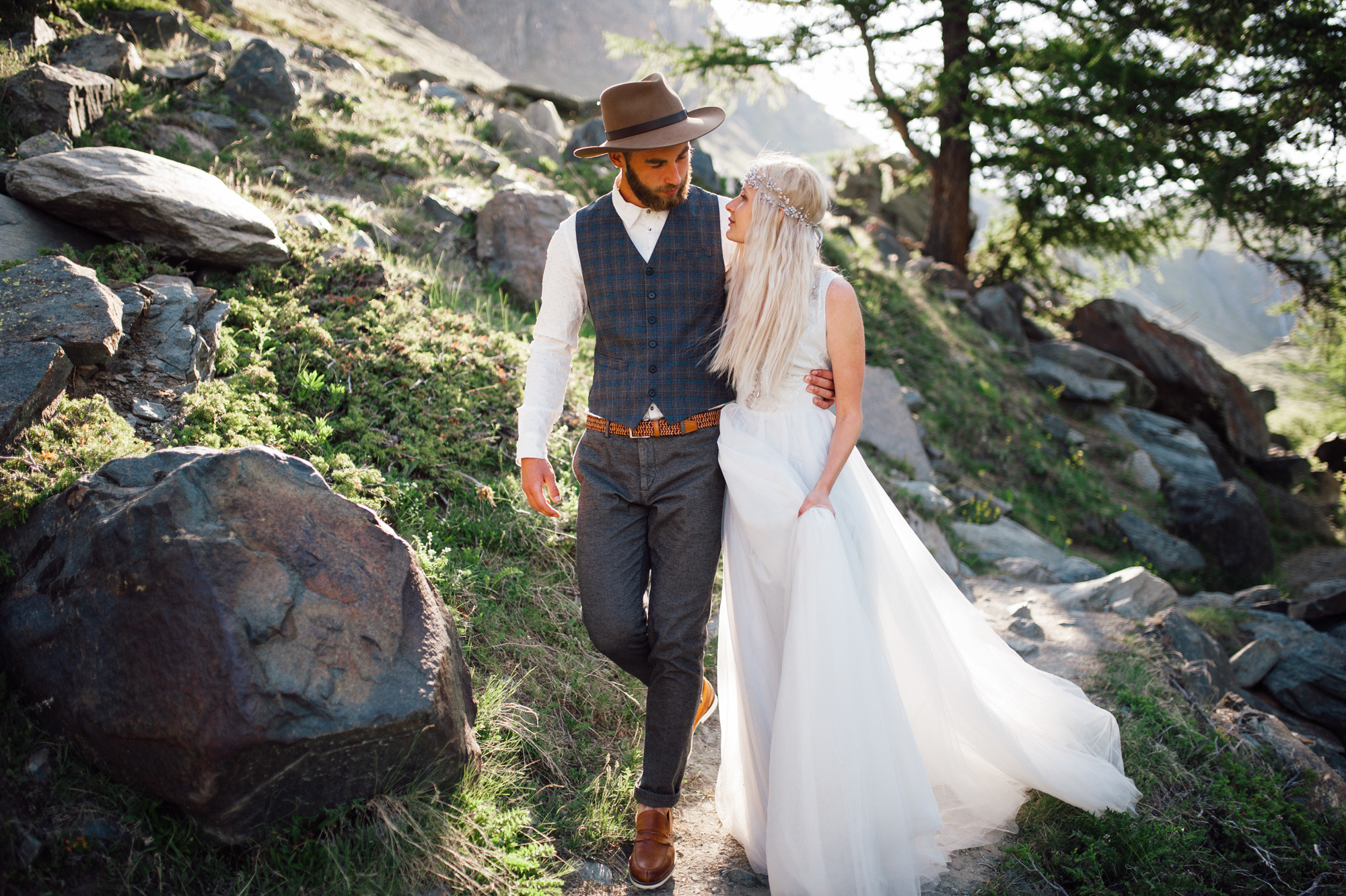 a bride and groom walking down a path in the mountains