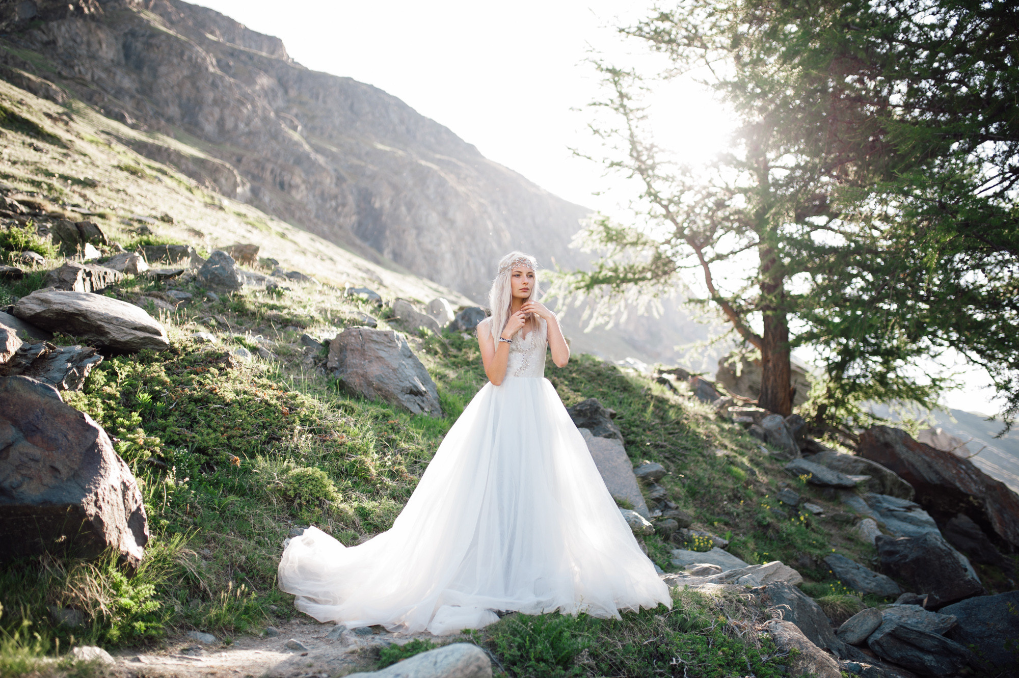 a bride in a wedding dress standing on a rocky hillside