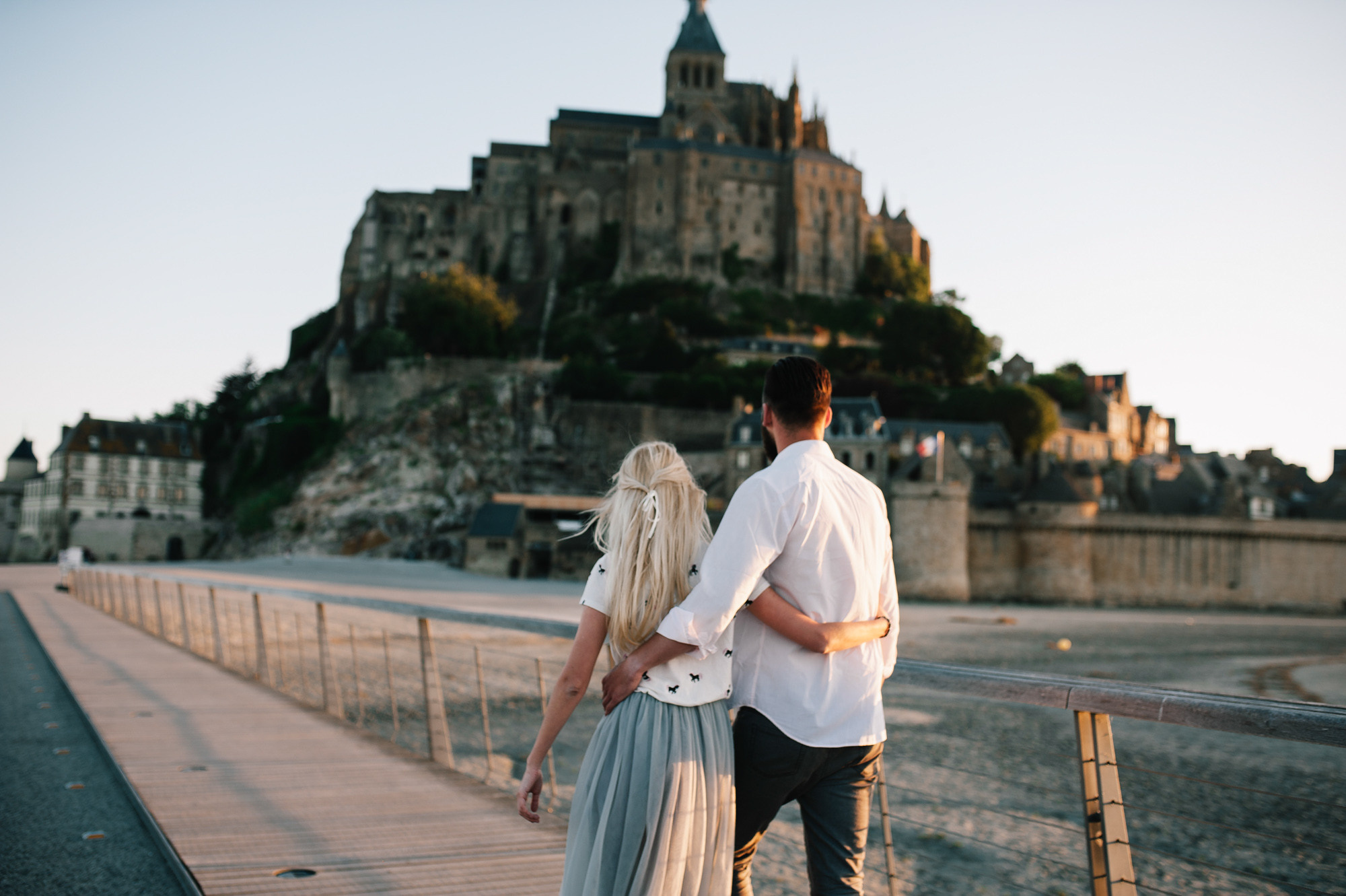 a couple walking on a bridge in front of a castle