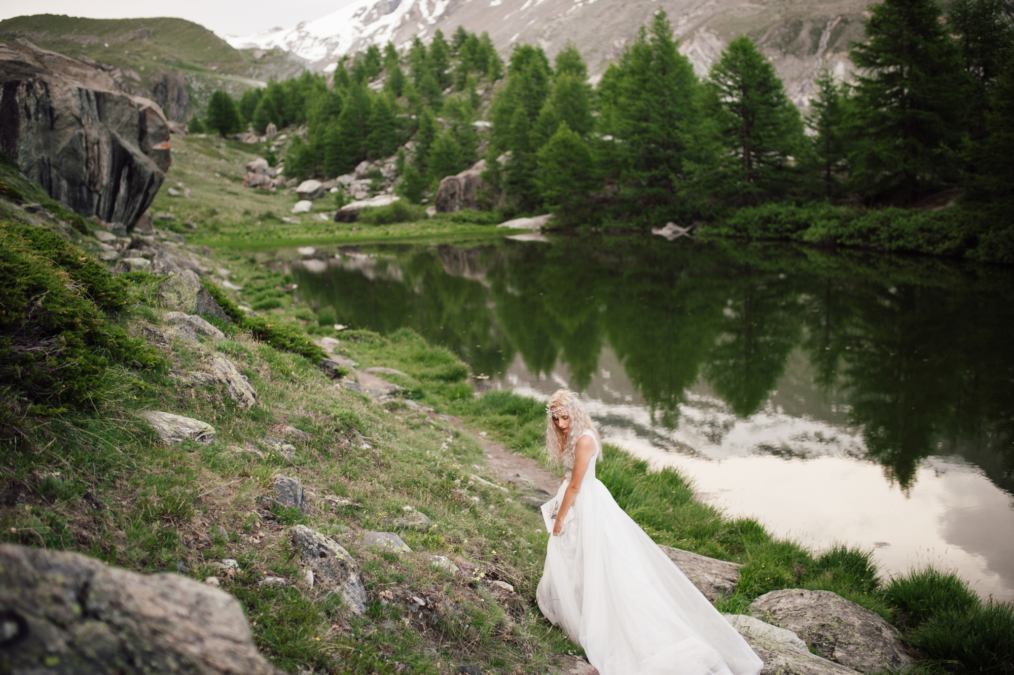 a bride standing on a rocky hillside by a lake