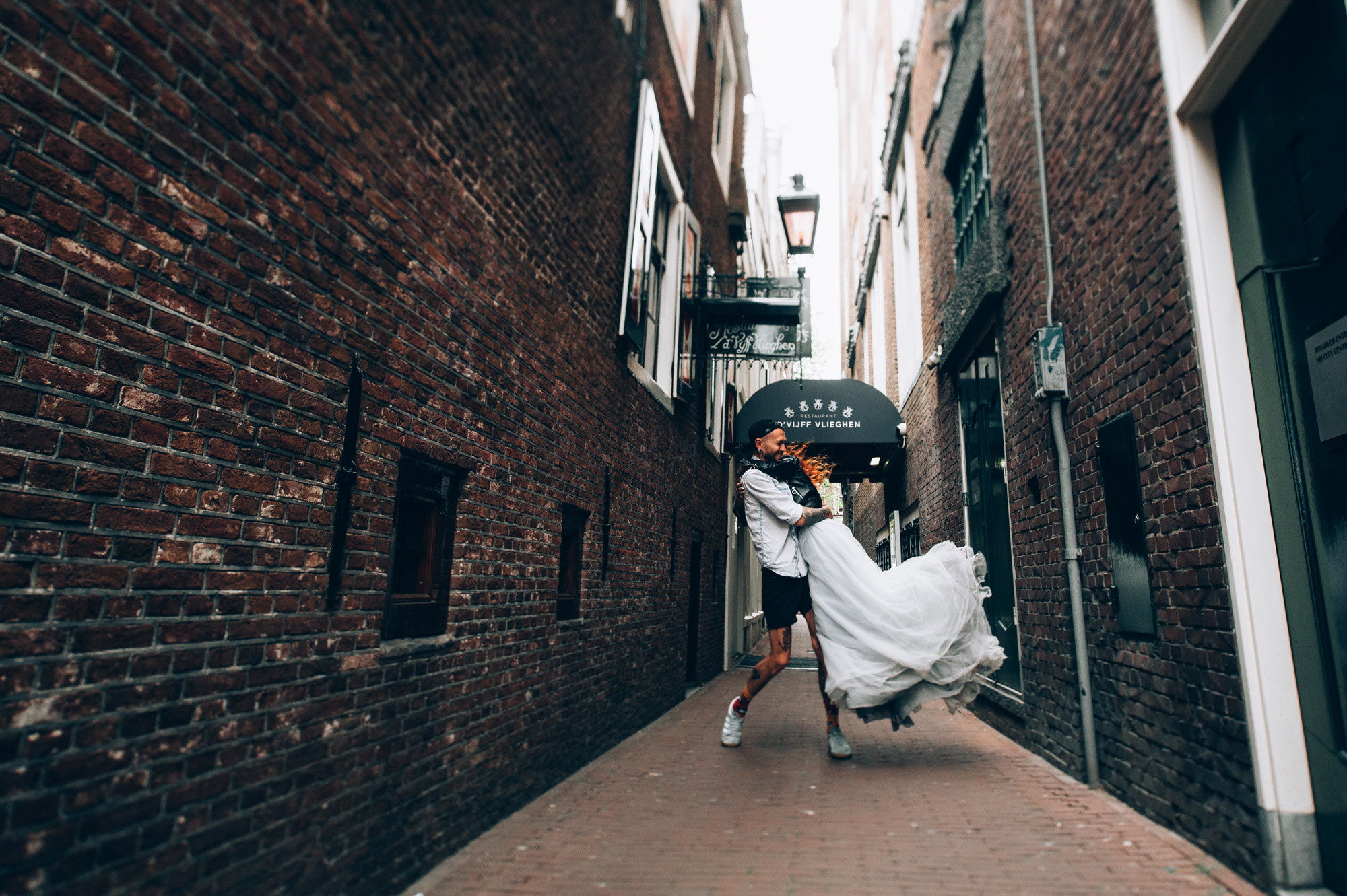 a woman in a white dress is walking down a narrow alley
