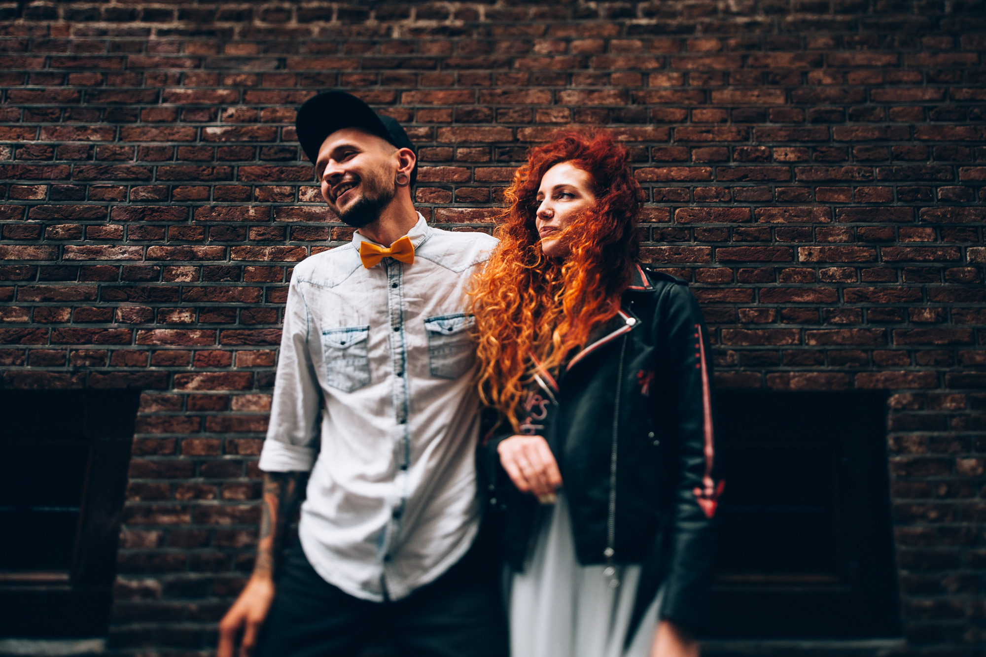 a man and woman standing next to a brick wall