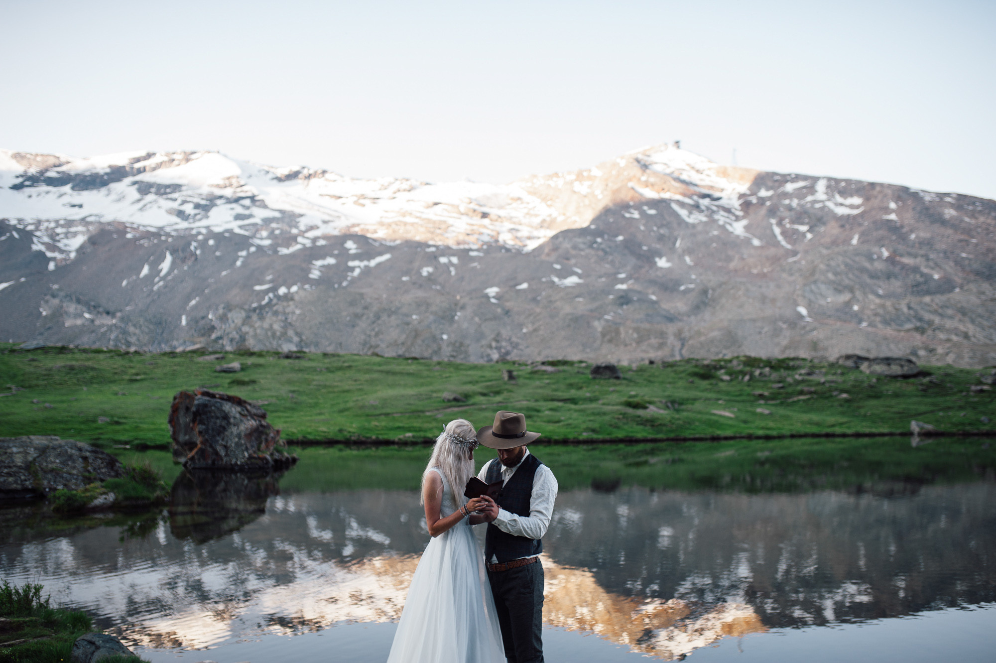 a bride and groom standing in front of a mountain lake
