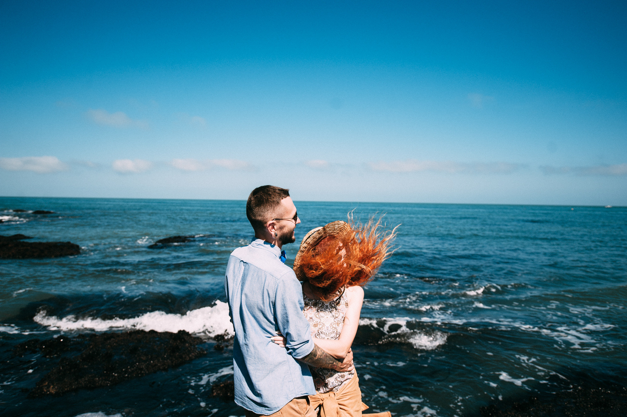 a man and woman standing on a rock by the ocean