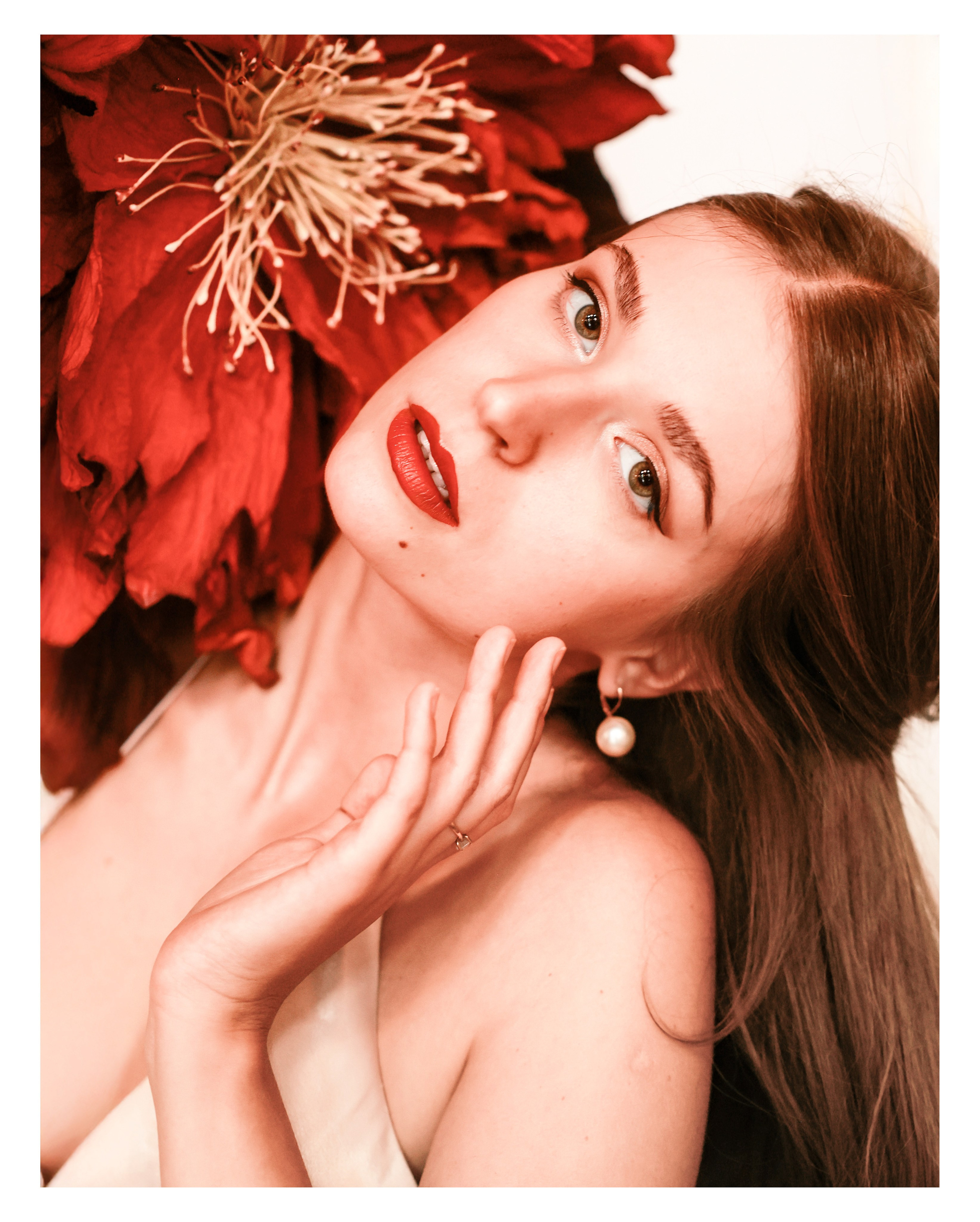 Frau mit offenem Rücken und langem Haar neben einer übergroßen roten Blume – künstlerische Fotografie einer Opernsängerin im Schloss Mirabell in Salzburg.