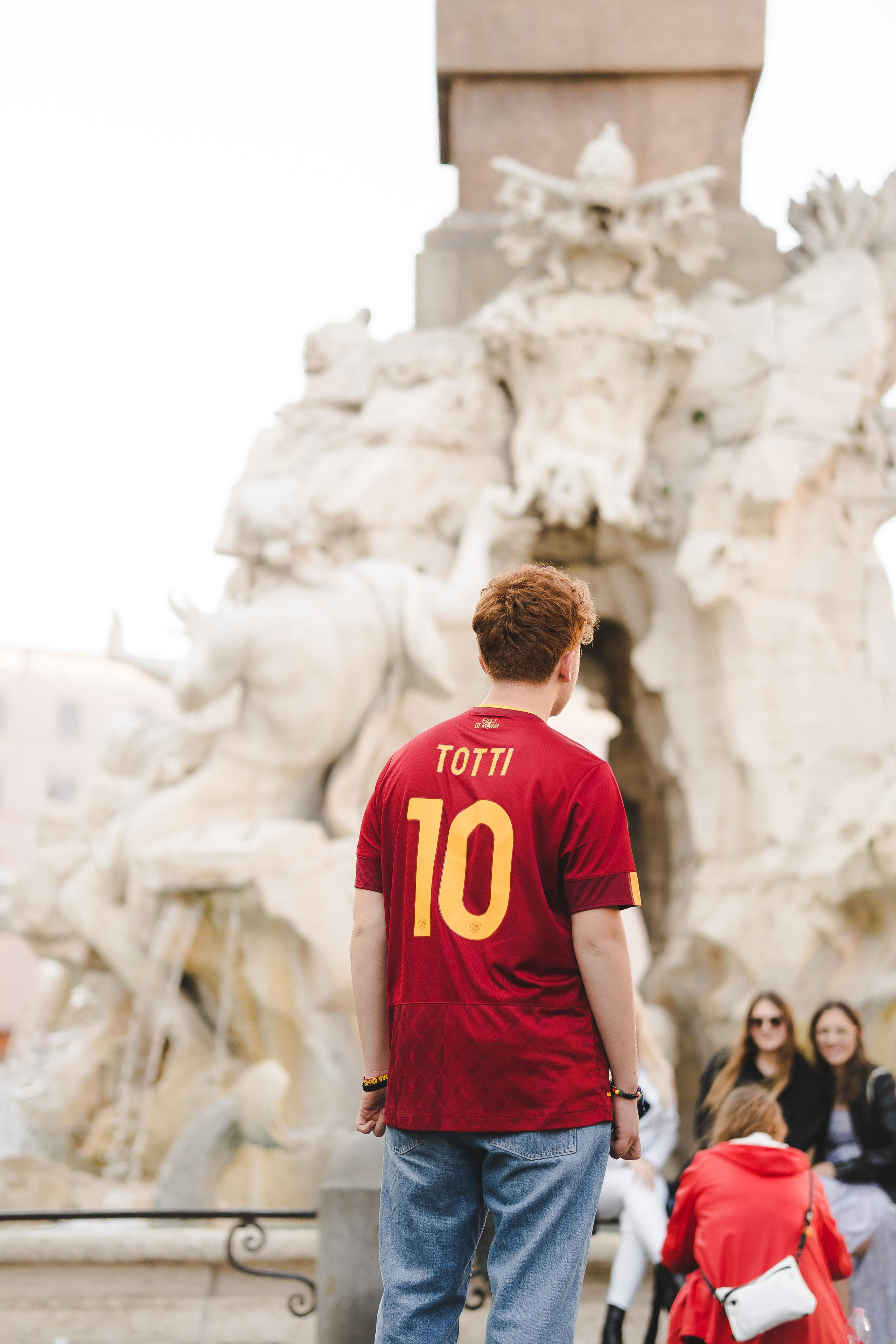 A boy wearing a red sports jersey standing and looking ahead
