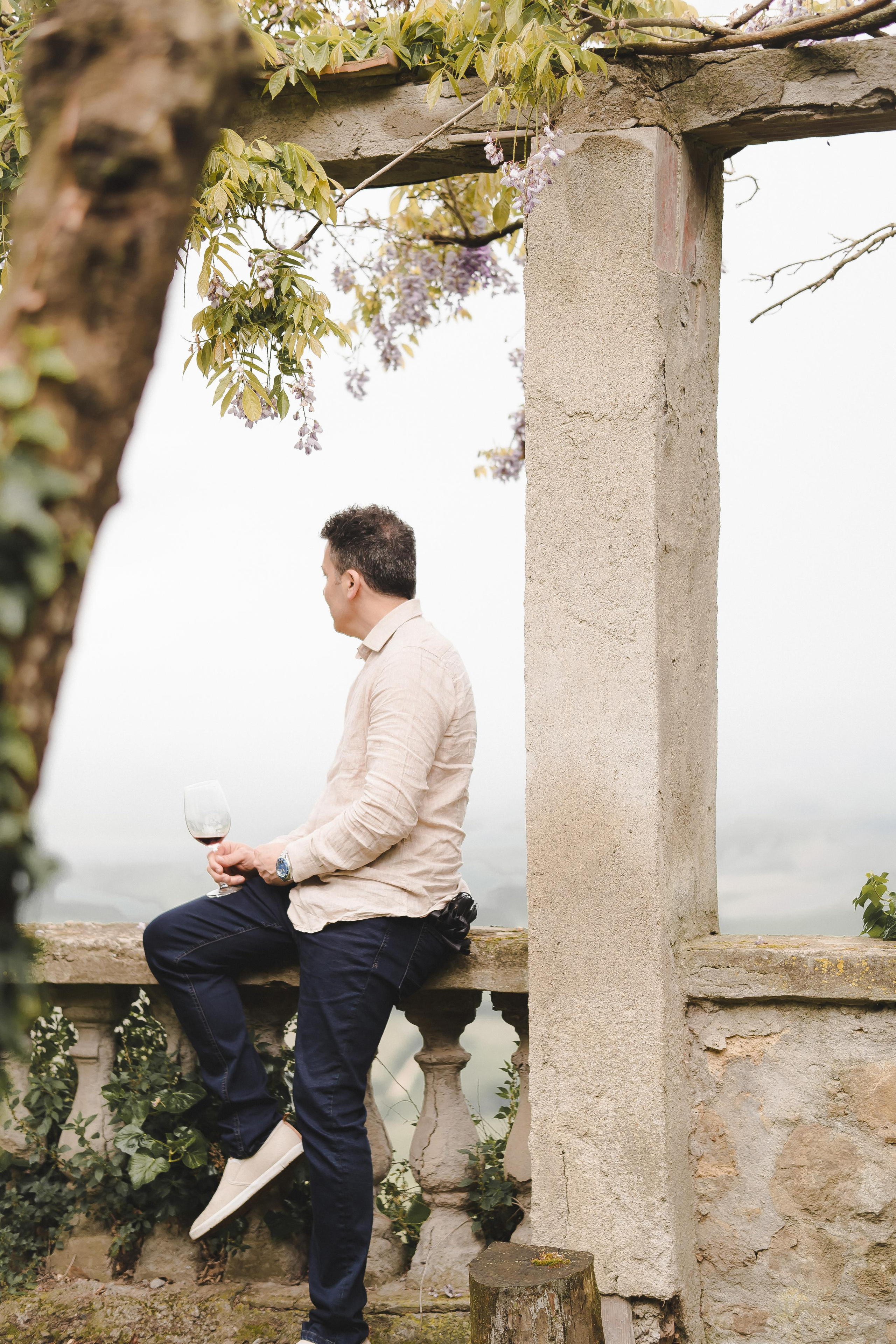Man holding wine glass at the edge of a cliff in Tuscany