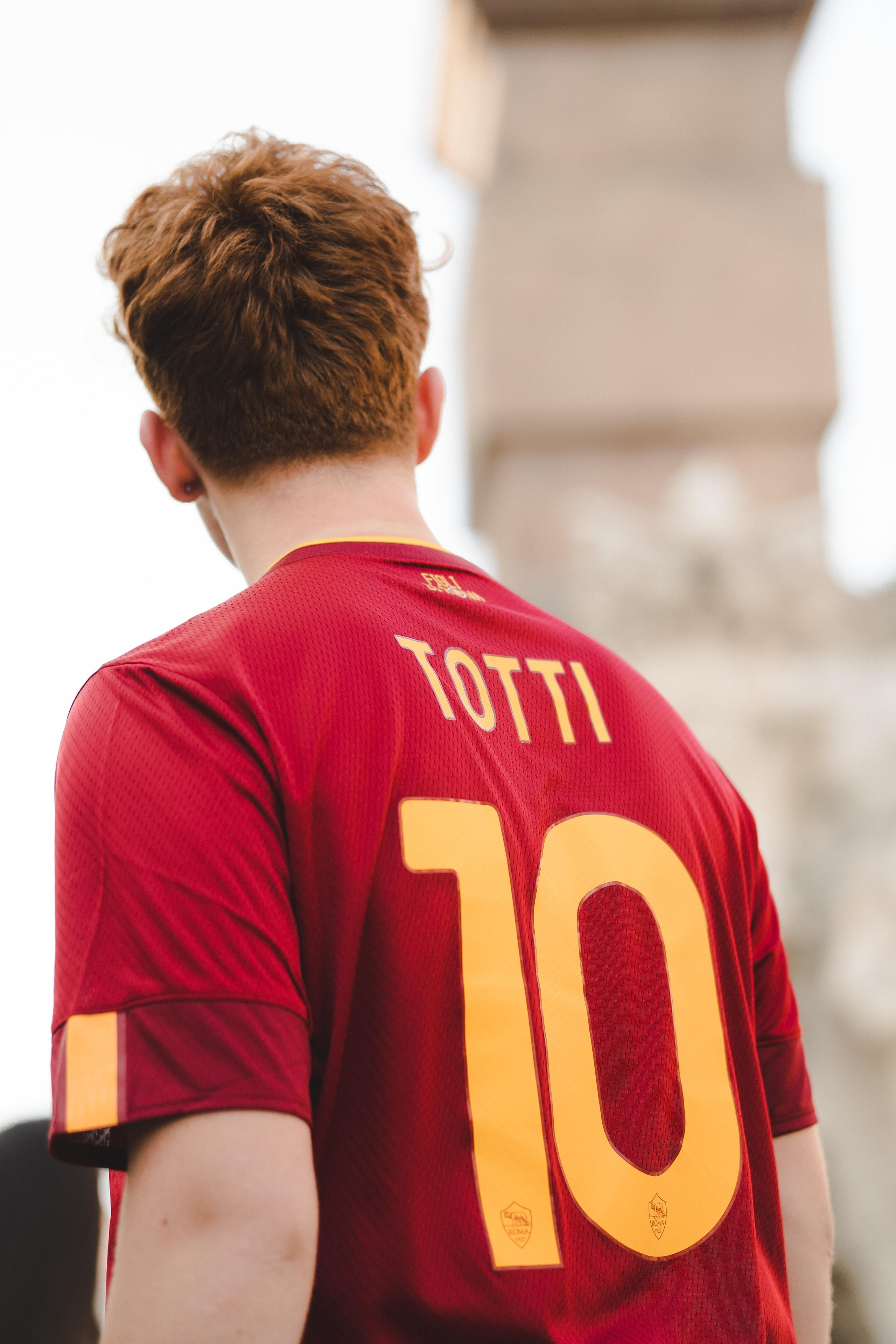 A boy wearing a red sports jersey standing and looking ahead