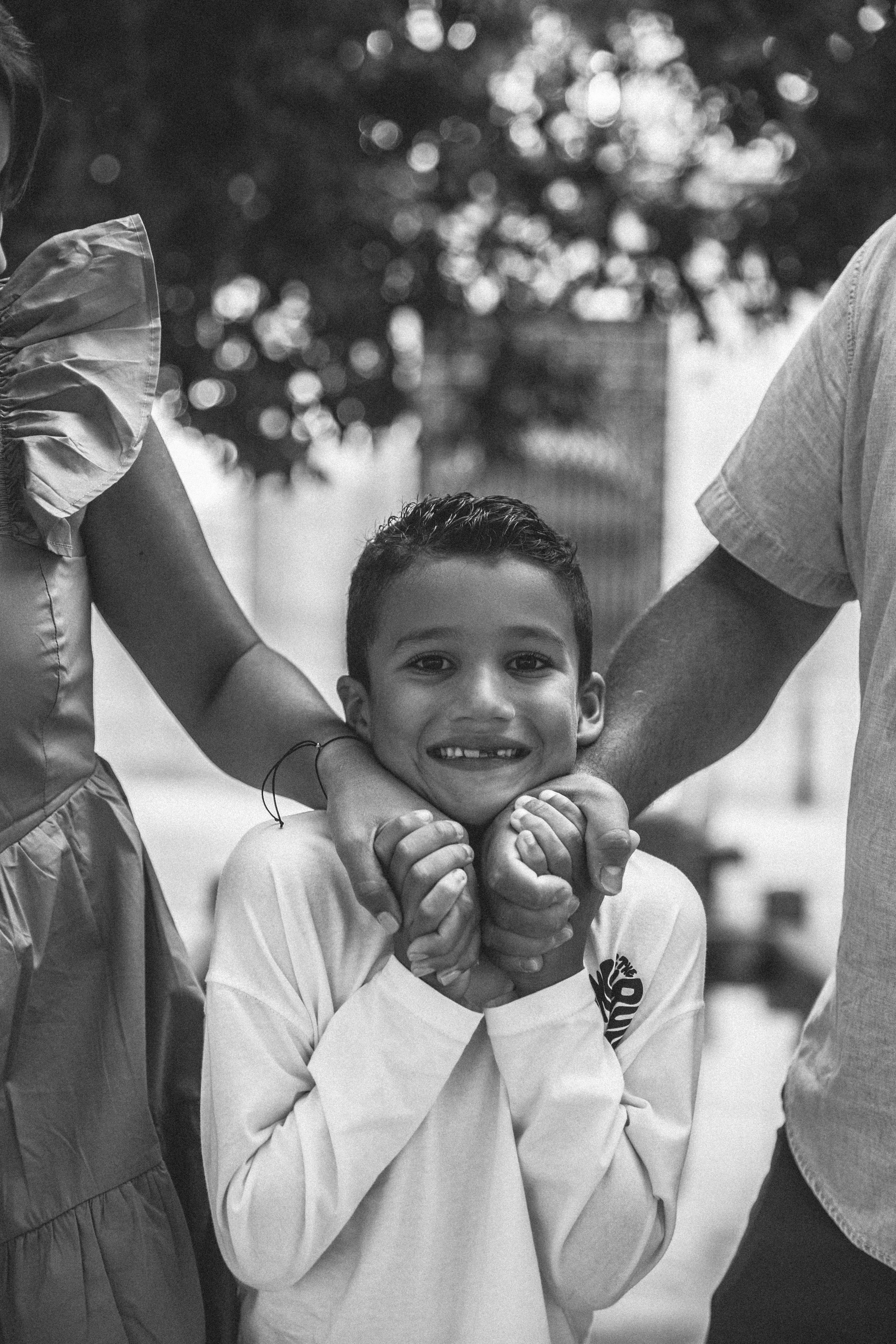 Retrato en blanco y negro de un niño sonriente sostenido por las manos de sus padres — capturando una conexión familiar íntima en las encantadoras calles de Valencia, España.
