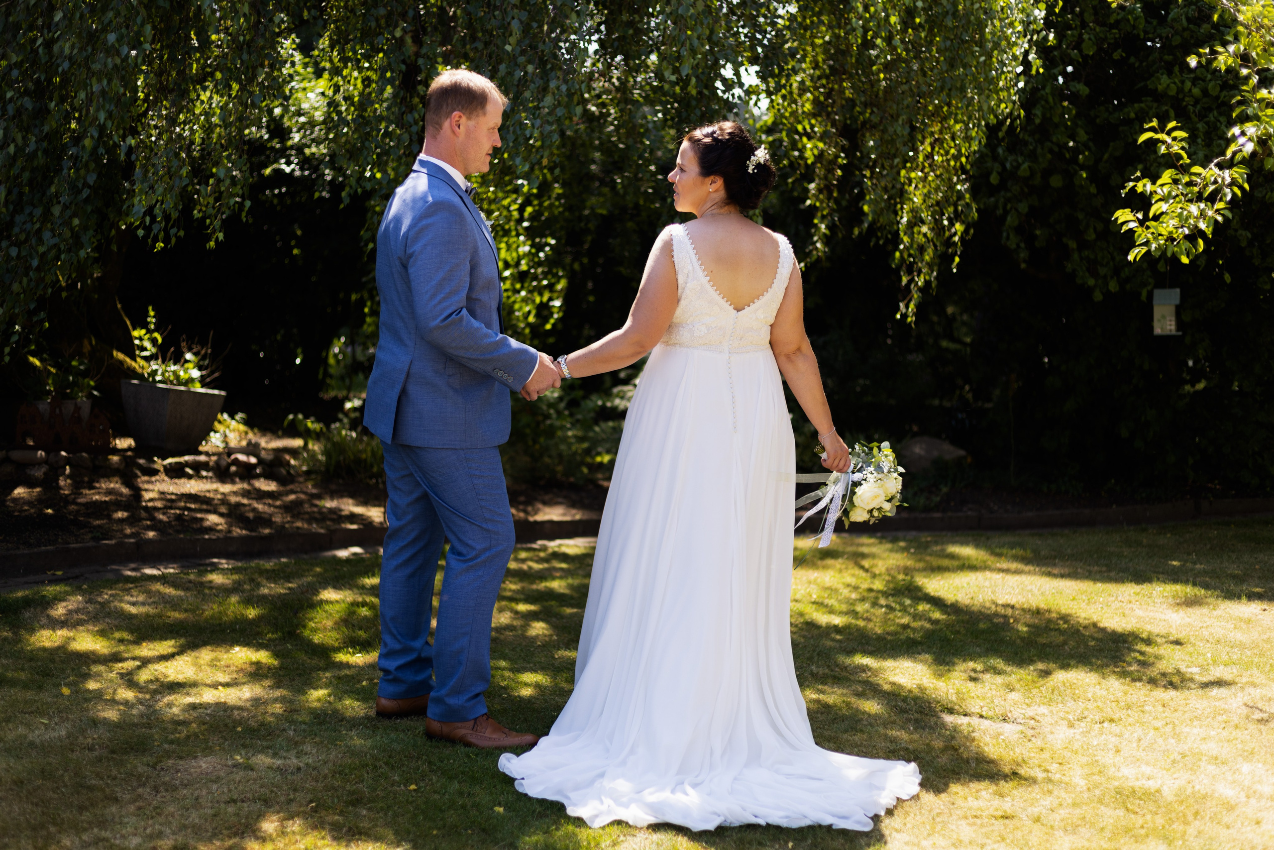Hochzeitsfoto auf einem Feld bei Sonnenuntergang, Brautpaar lehnt an Strohballen in ländlicher Idylle.