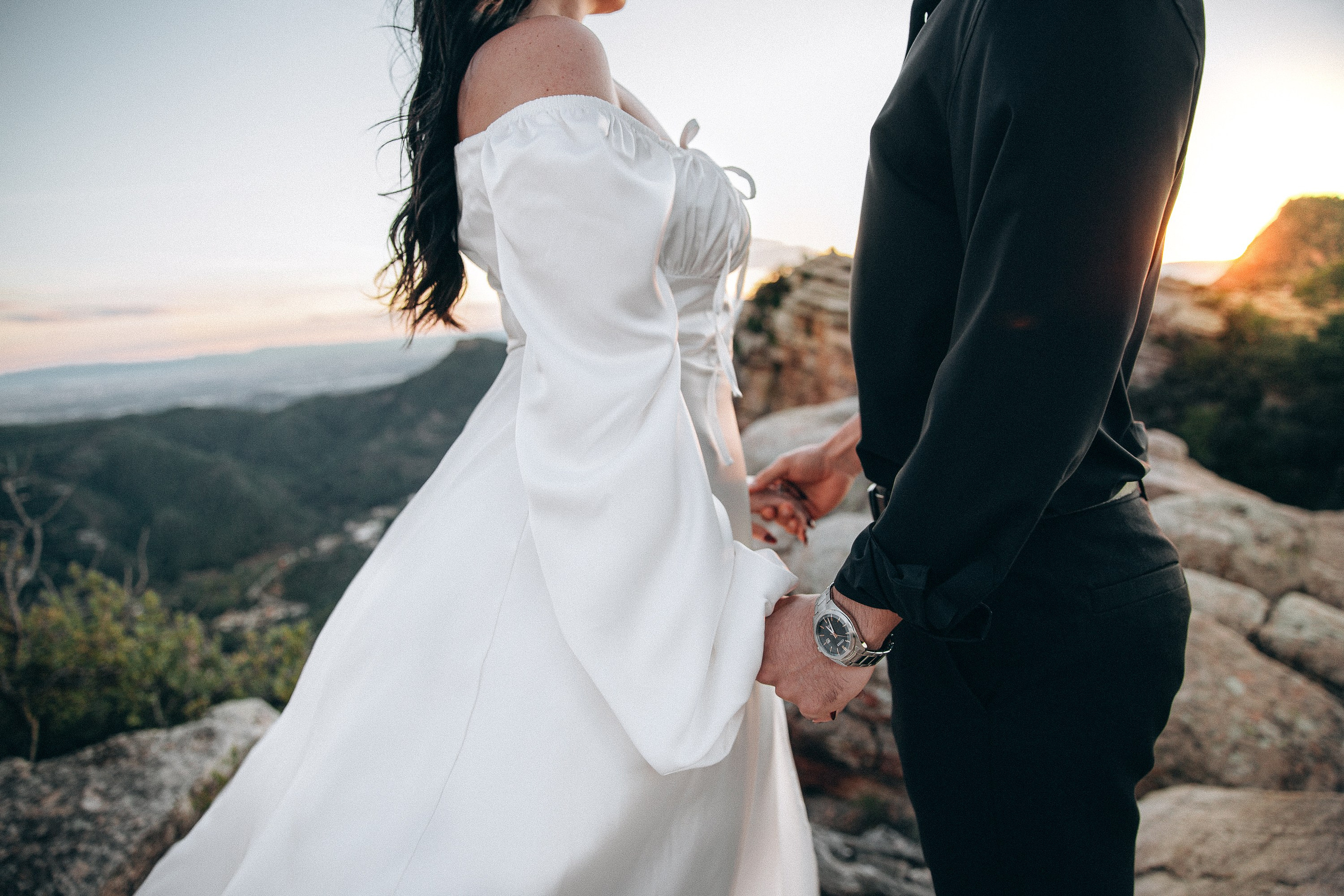 Close-up of bride’s flowing white dress and couple holding hands on a scenic mountain overlook during a destination elopement in Barcelona, Spain. This elegant detail shot highlights the intimacy of a small civil wedding in nature.