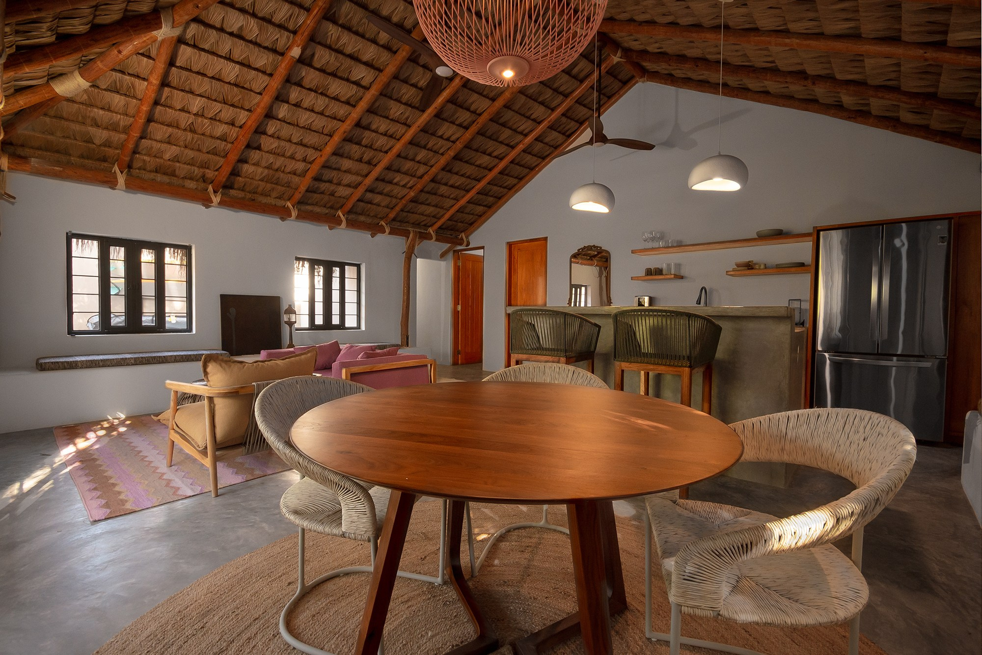 Coastal style dining area in San Jose del Cabo – wooden table, palm thatched ceiling and open kitchen layout, luxury home photography