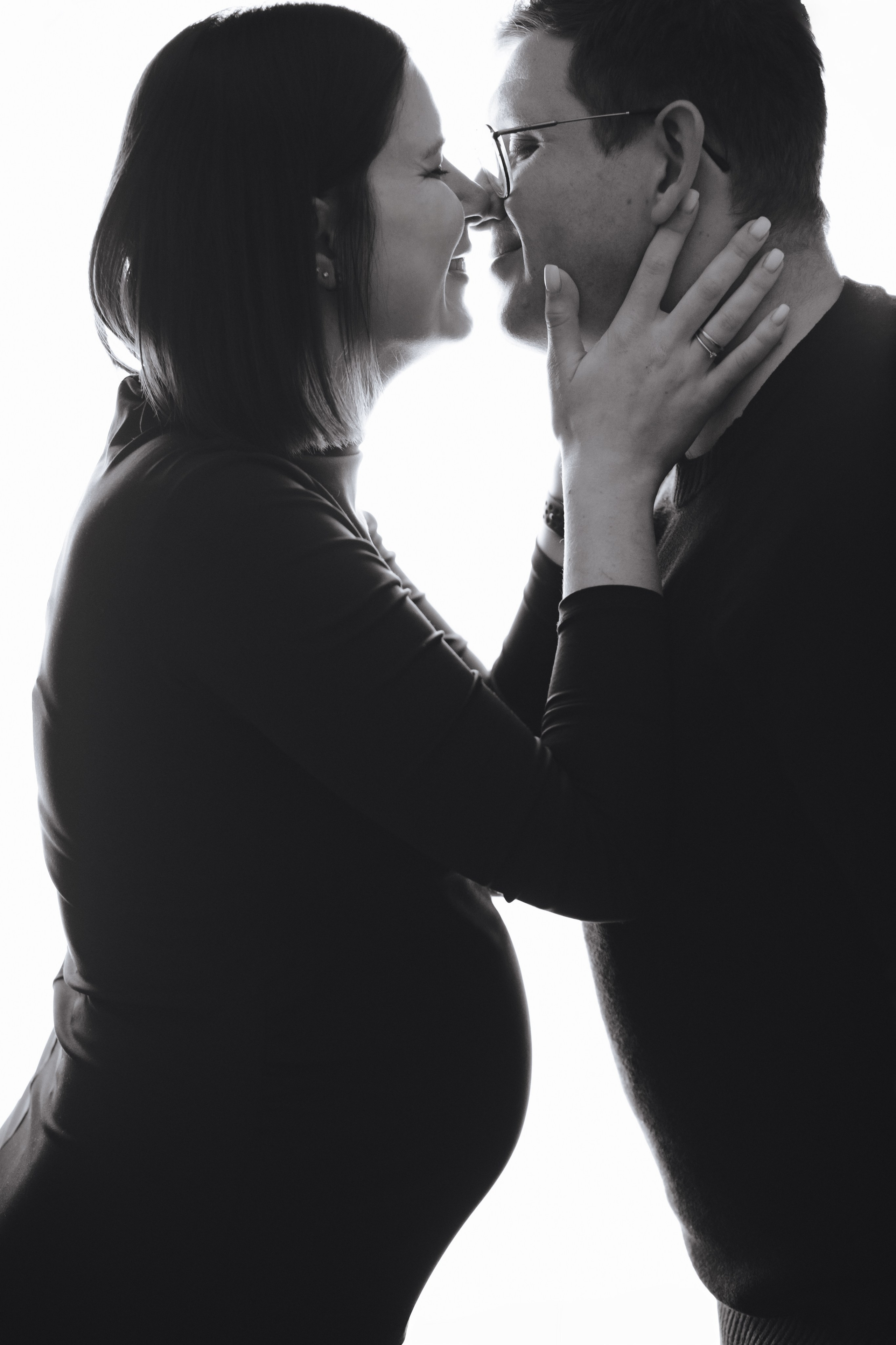 Schwangere Frau küsst ihren Mann, während ihr Babybauch als Silhouette im Fotostudio in Hausen sichtbar ist.