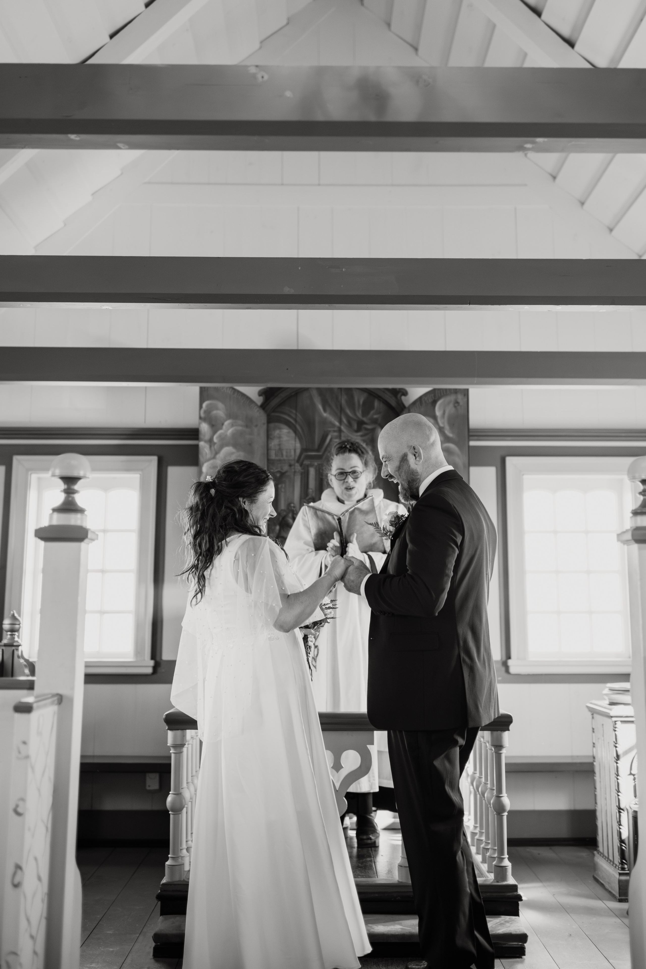 Intimate embrace between the bride and groom near the black church of Búðir, framed by rolling hills and an overcast sky.