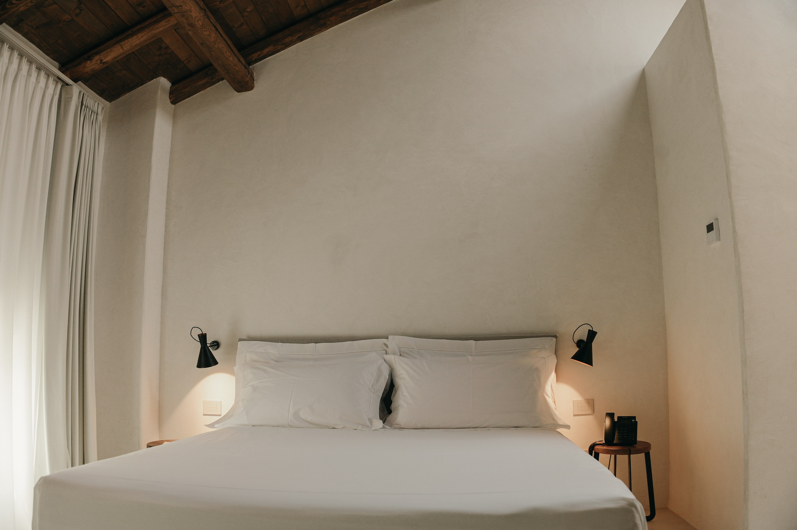 Minimalist double bedroom with soft lighting and rustic wooden ceiling in a boutique accommodation