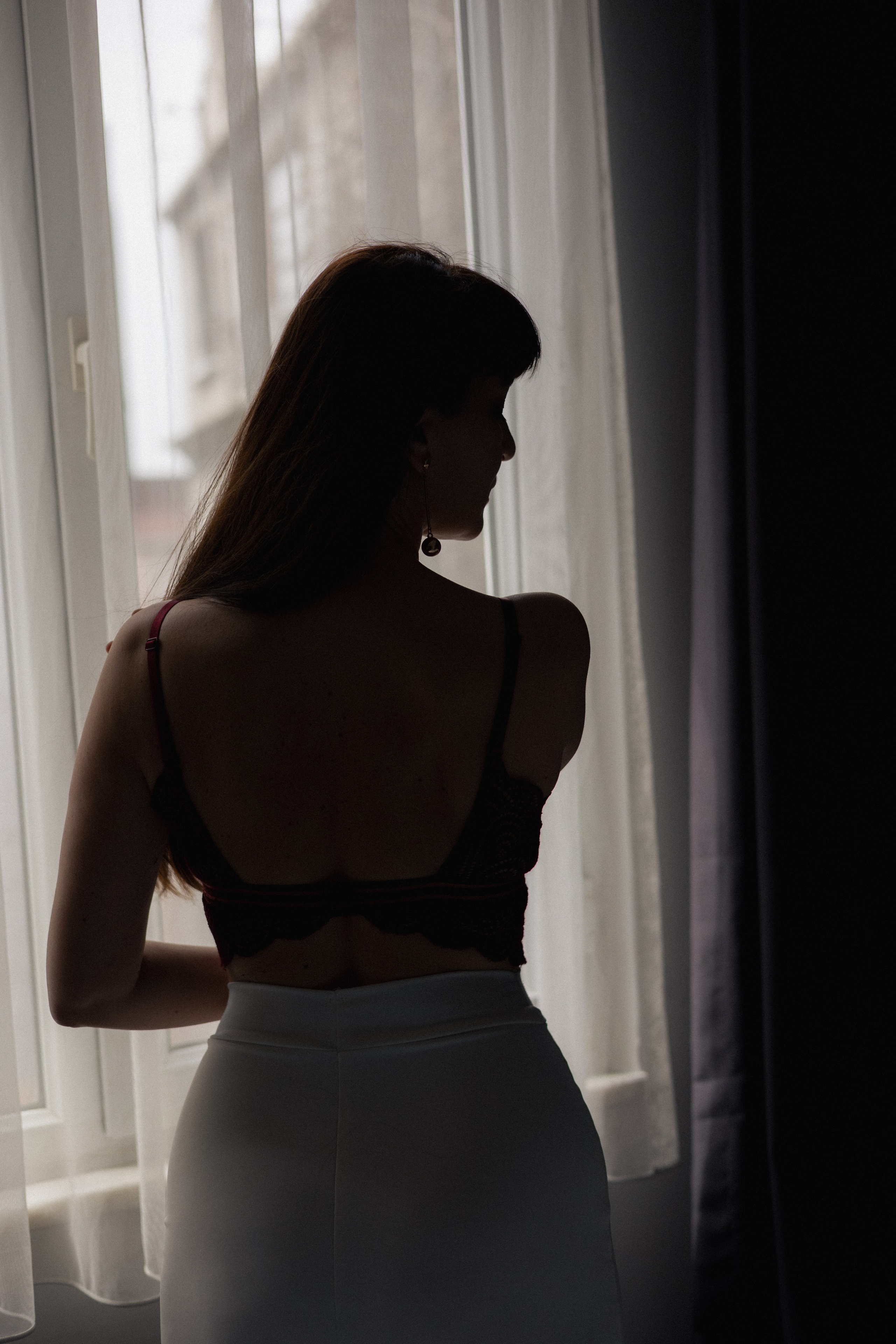 Женский силуэт у окна с полупрозрачной занавеской, мягкий контровый свет и спокойное настроение
