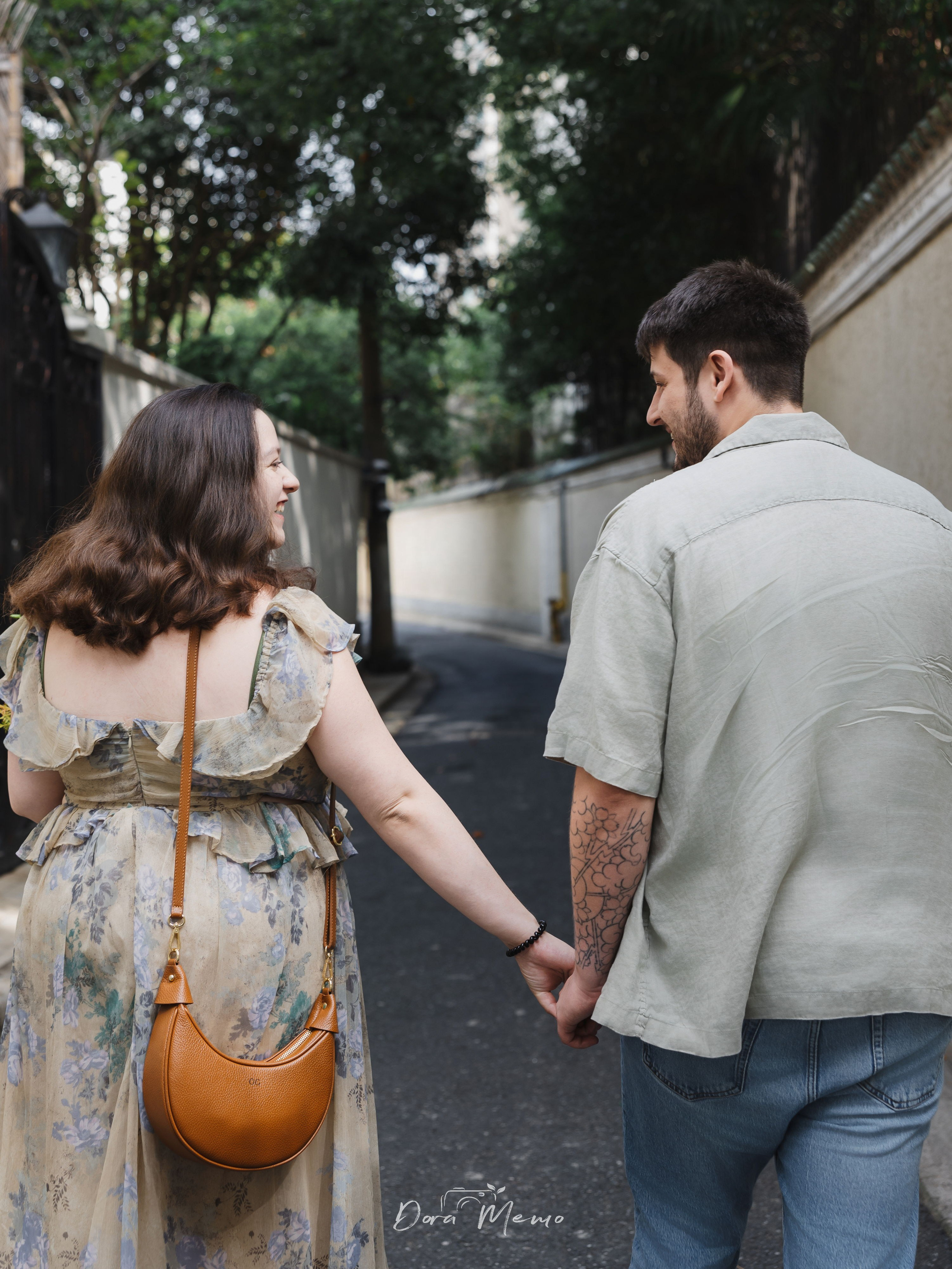 A couple holding hands while walking through the leafy streets of Shanghai during a relaxed pregnancy photo session.