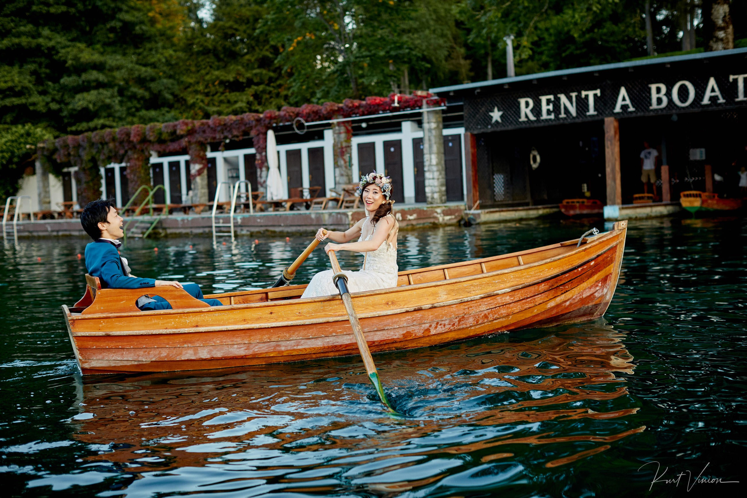 Strong bride rowing groom rowboat back Vila Bled dock sunset.