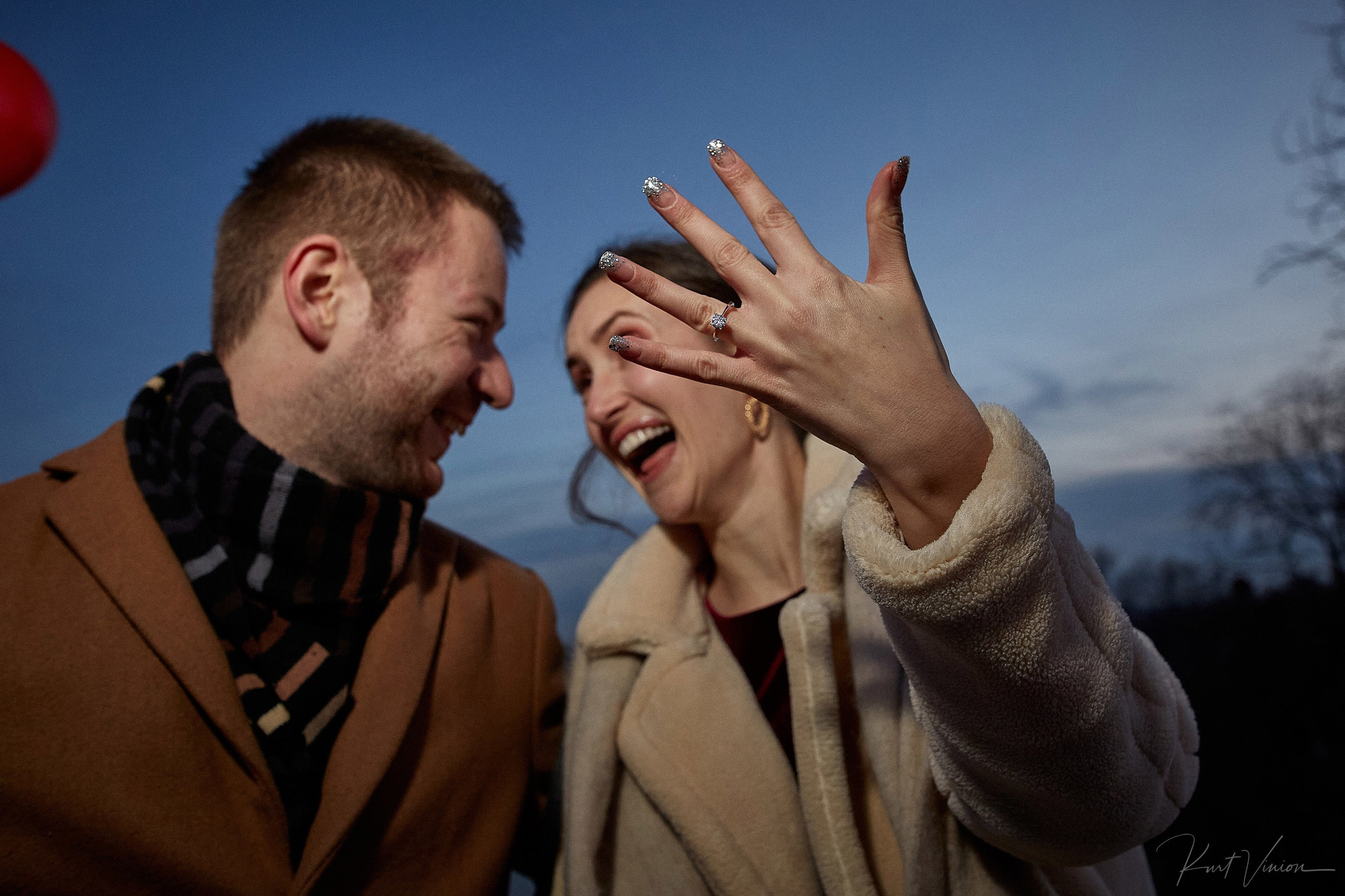 Exuberent woman smiles towards her partner as she proudly showcases her diamand engagement ring