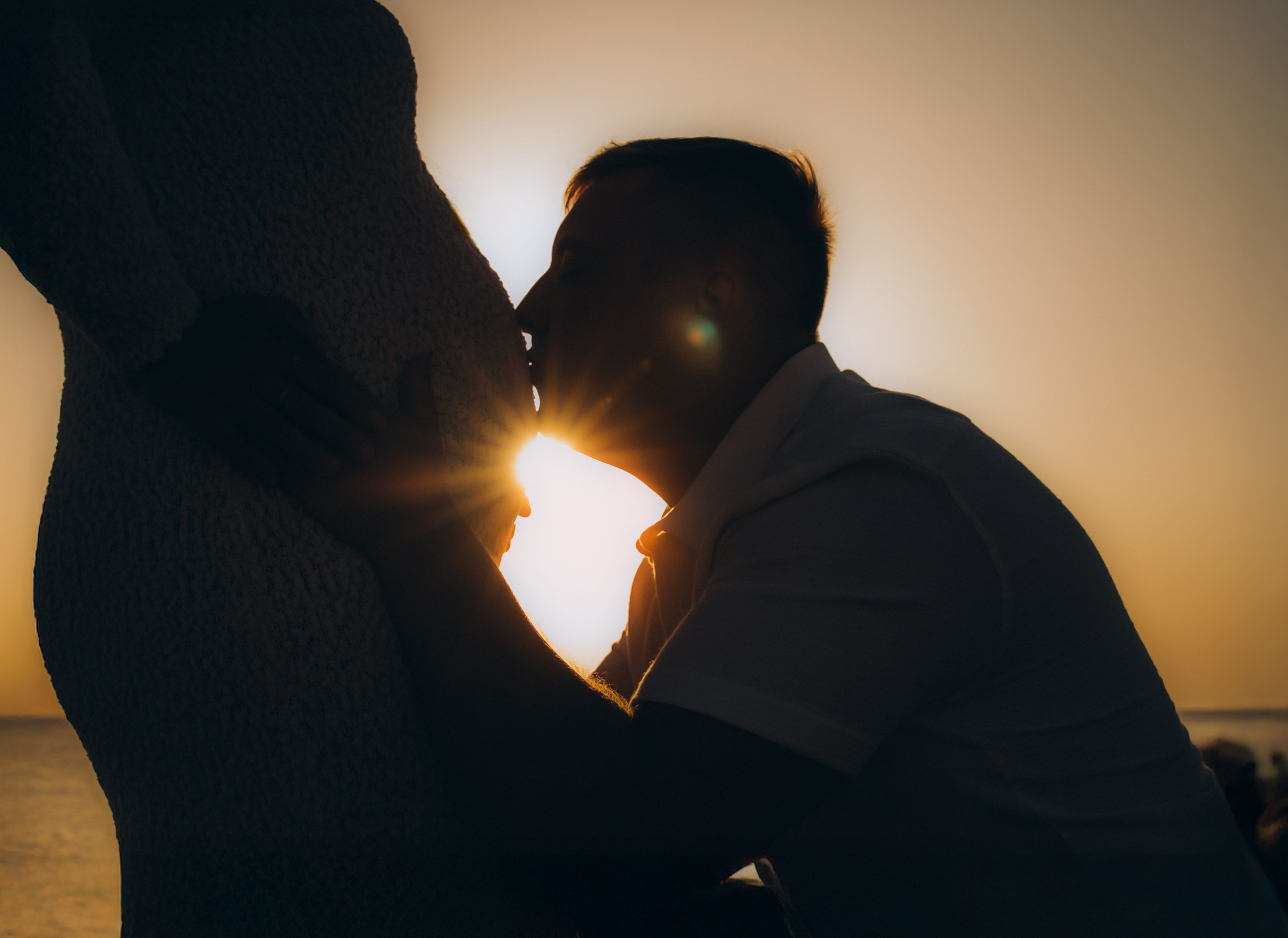 Foto artística en silueta en Barcelona, España — pareja formando un corazón con las manos alrededor de la barriga iluminada por el sol al atardecer. Sesión creativa y emocional capturando amor, ilusión y la magia de la maternidad en Barcelona.