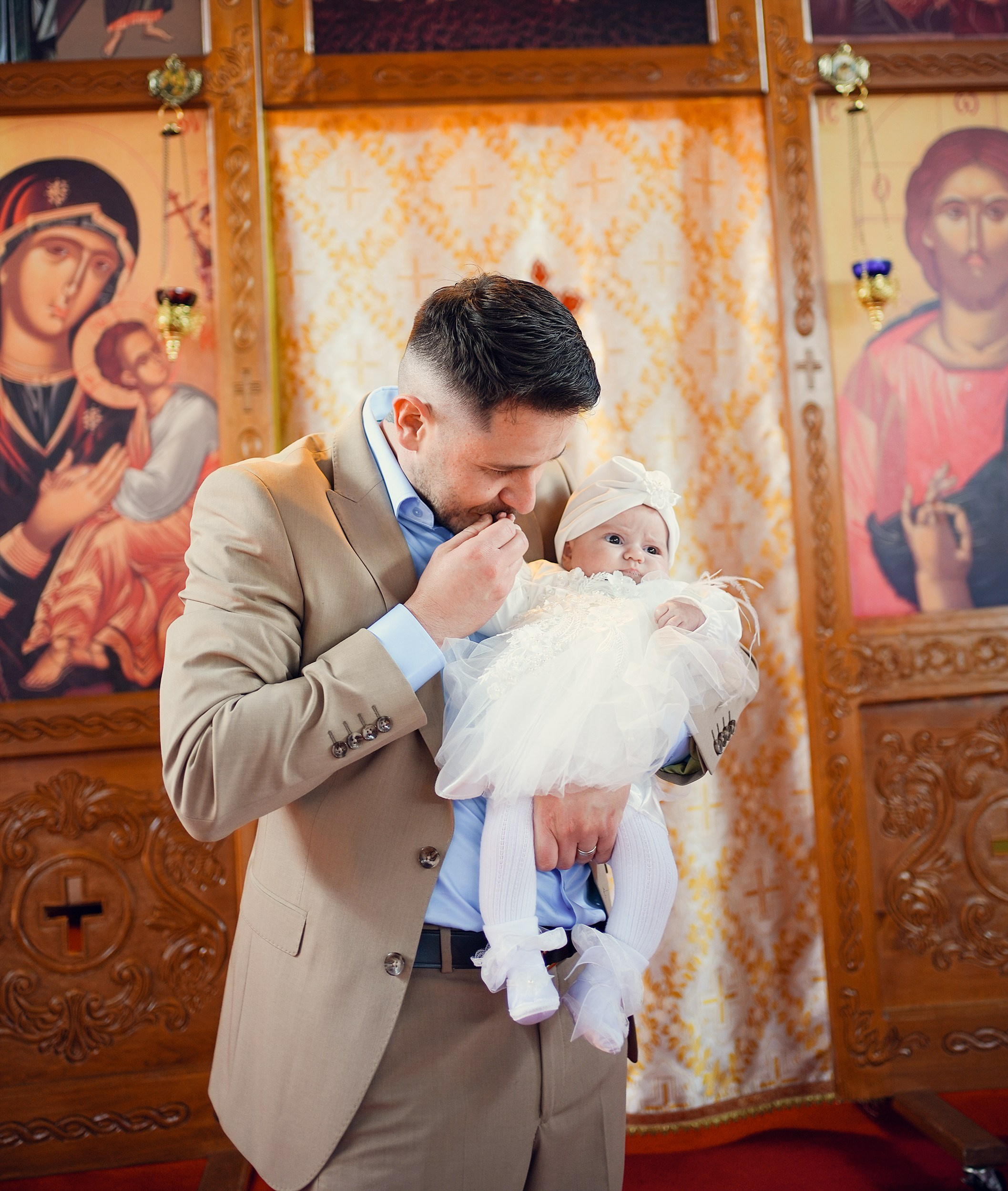 Father gently kissing his baby during the christening ceremony.