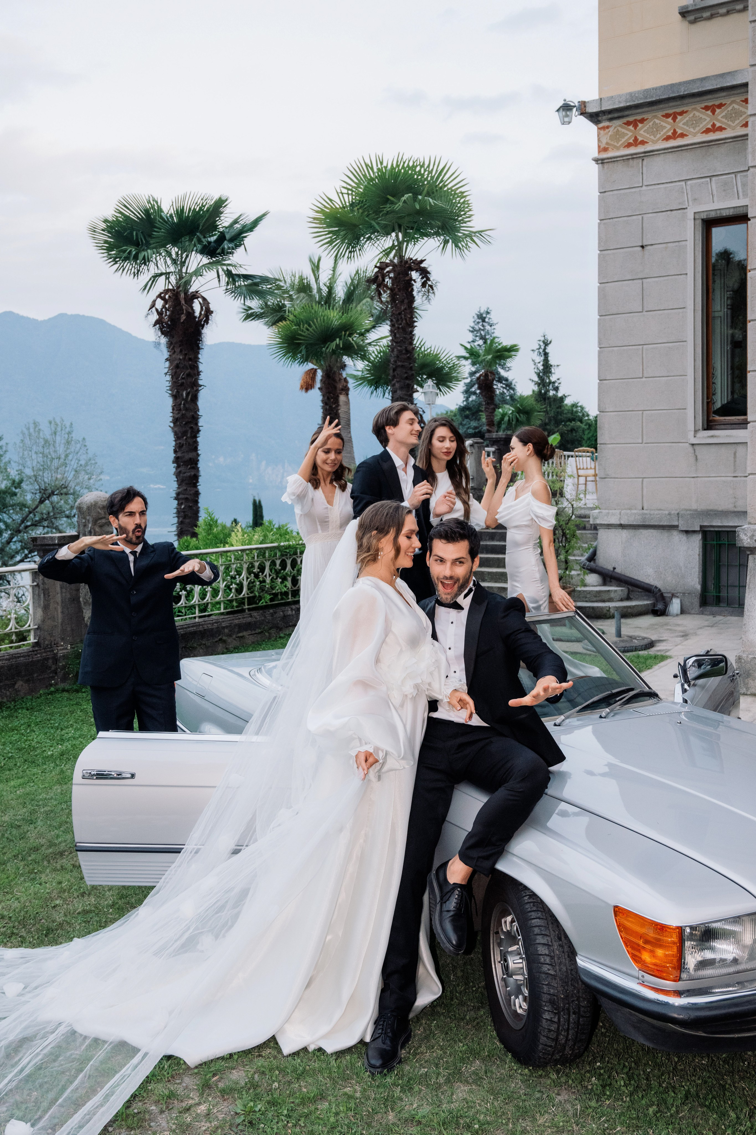 a bride and groom posing in front of a silver car
