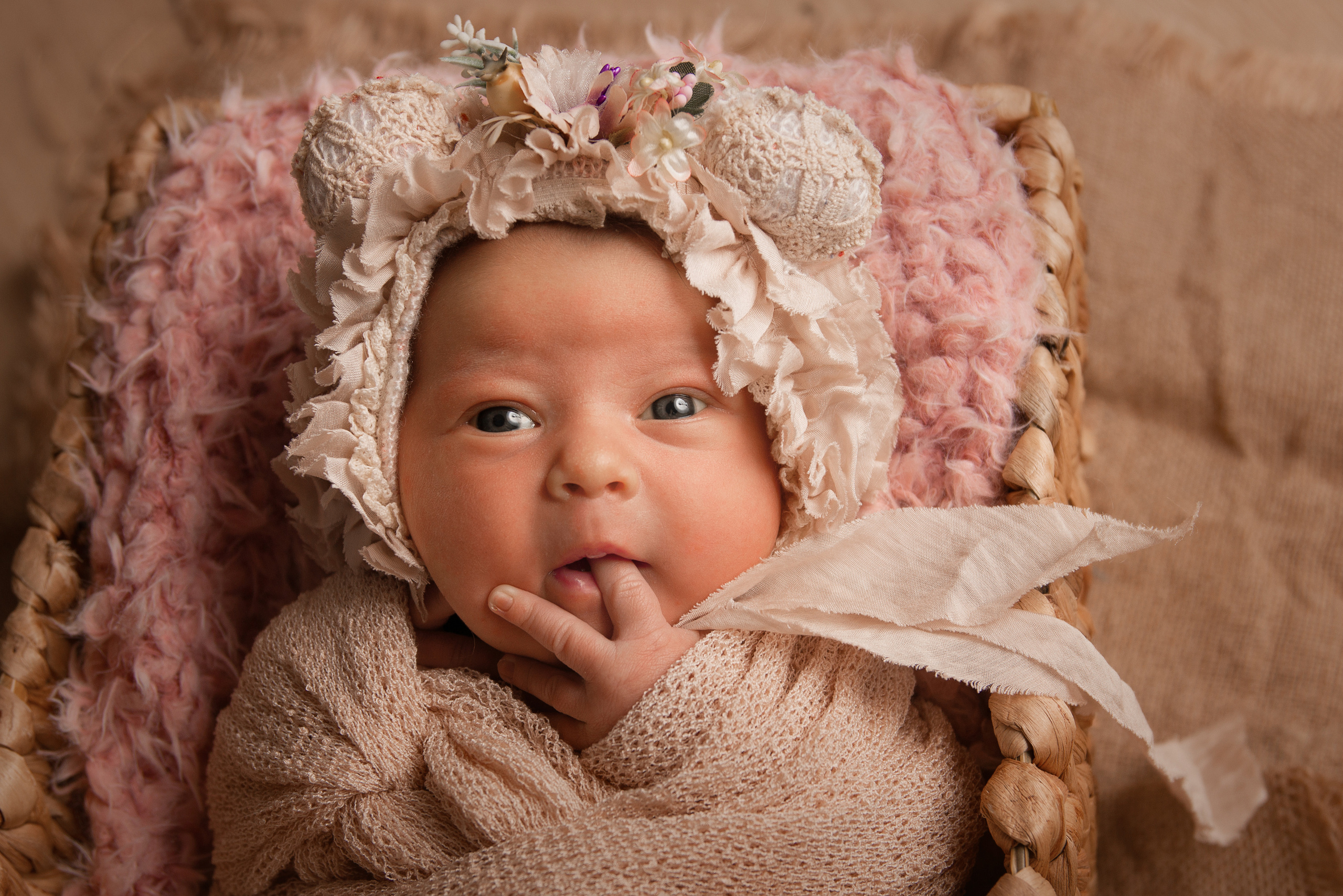 Neugeborenes mit Mütze zieht einen Finger in den Mund
