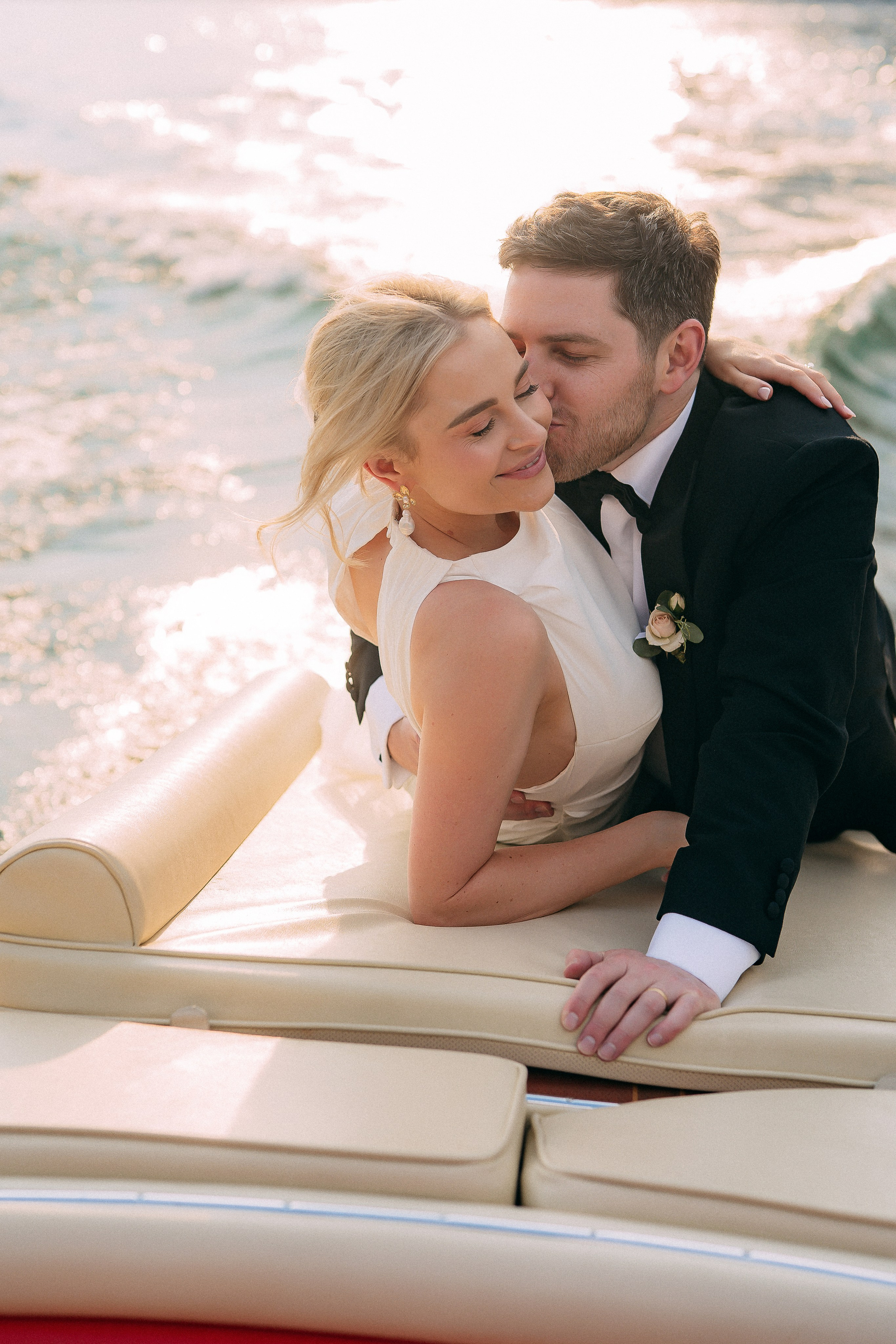 Bride and groom kissing on the boat at sunset near Villa Lario, Lake Como, Italy