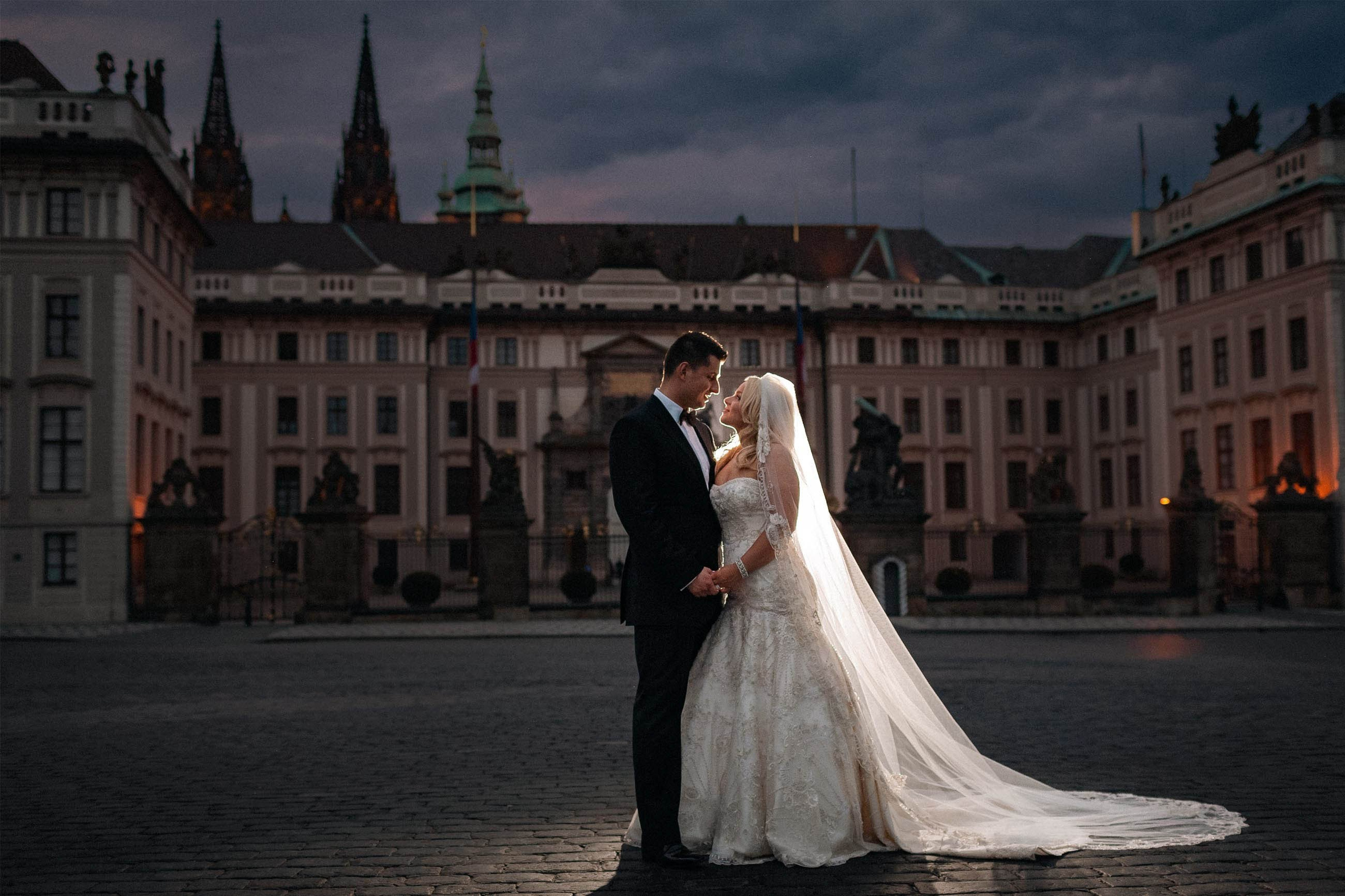Newlyweds enjoy a quiet moment in front of the historic main gates of Prague Castle on the night of their destination wedding