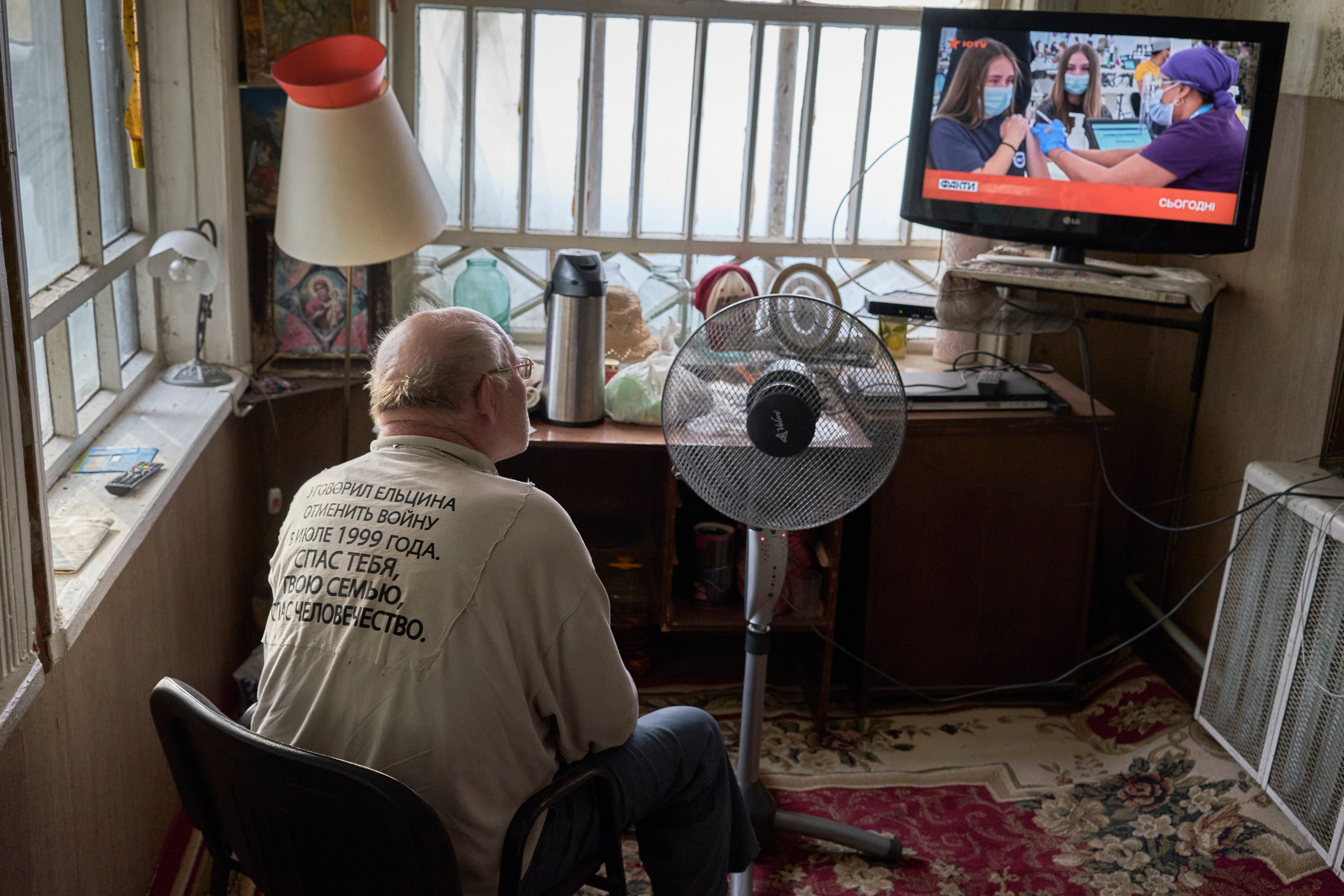 Viacheslav Veselov (aka ‘Kotik’ — ‘kitty’ from Russian) is watching local news on TV at home. The inscription on his shirt says: «Convinced Yeltsin to cancel the war in July 1999. Saved yourself, your family, saved humanity.»