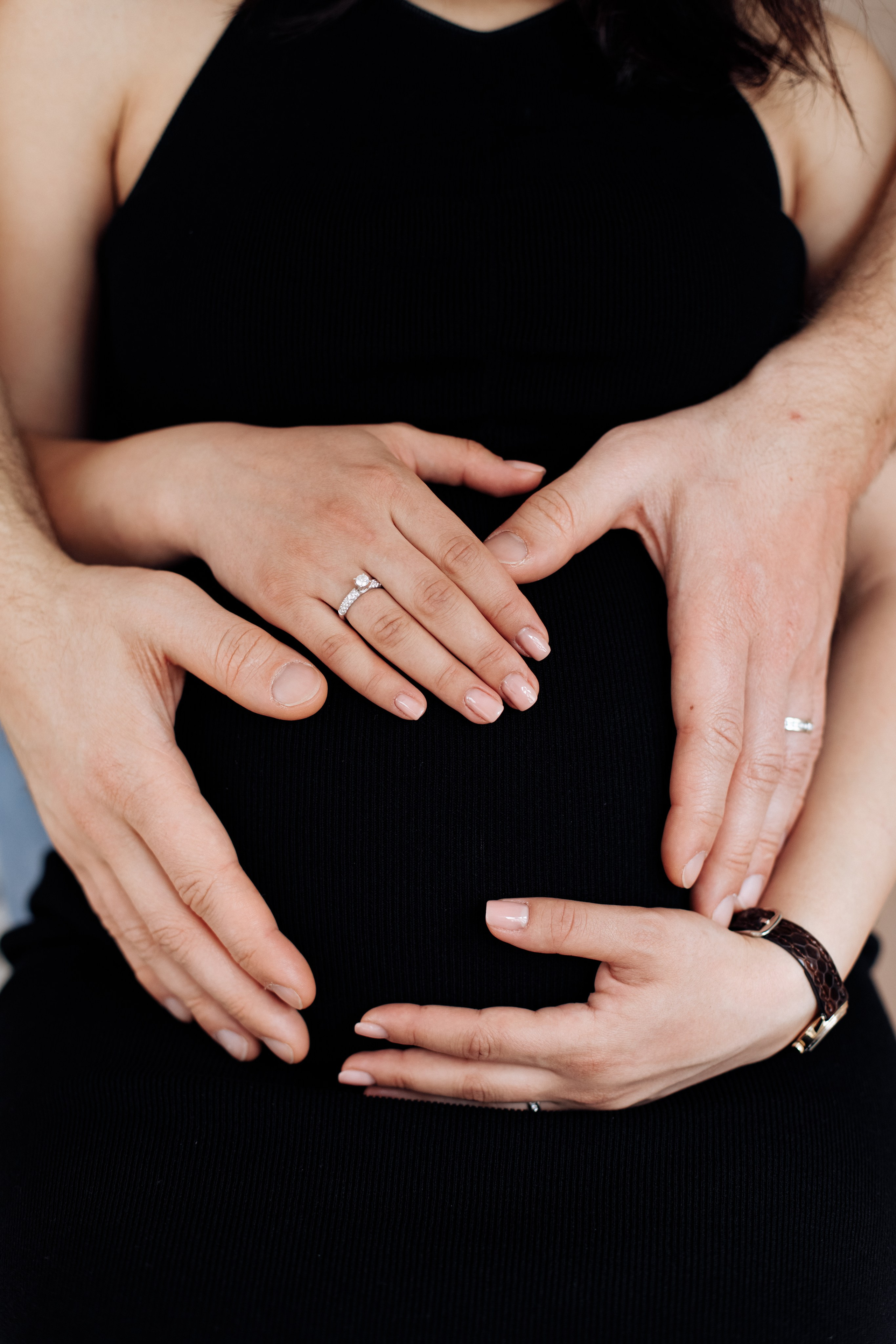 Hände von Mann und Frau liegen gemeinsam auf dem Babybauch der schwangeren Frau.