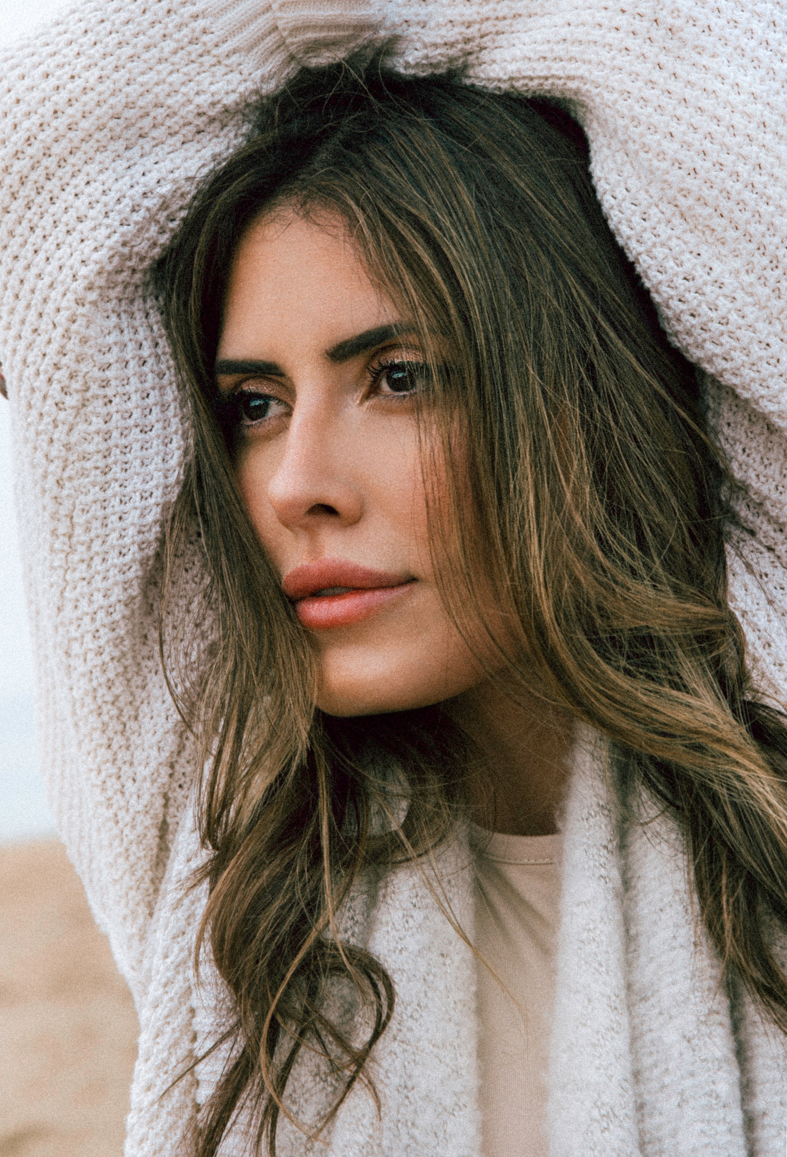 Крупный портрет женщины в уютном вязаном свитере с растрепанными волосами, задумчиво смотрящей на пляже в Валенсии, Испания