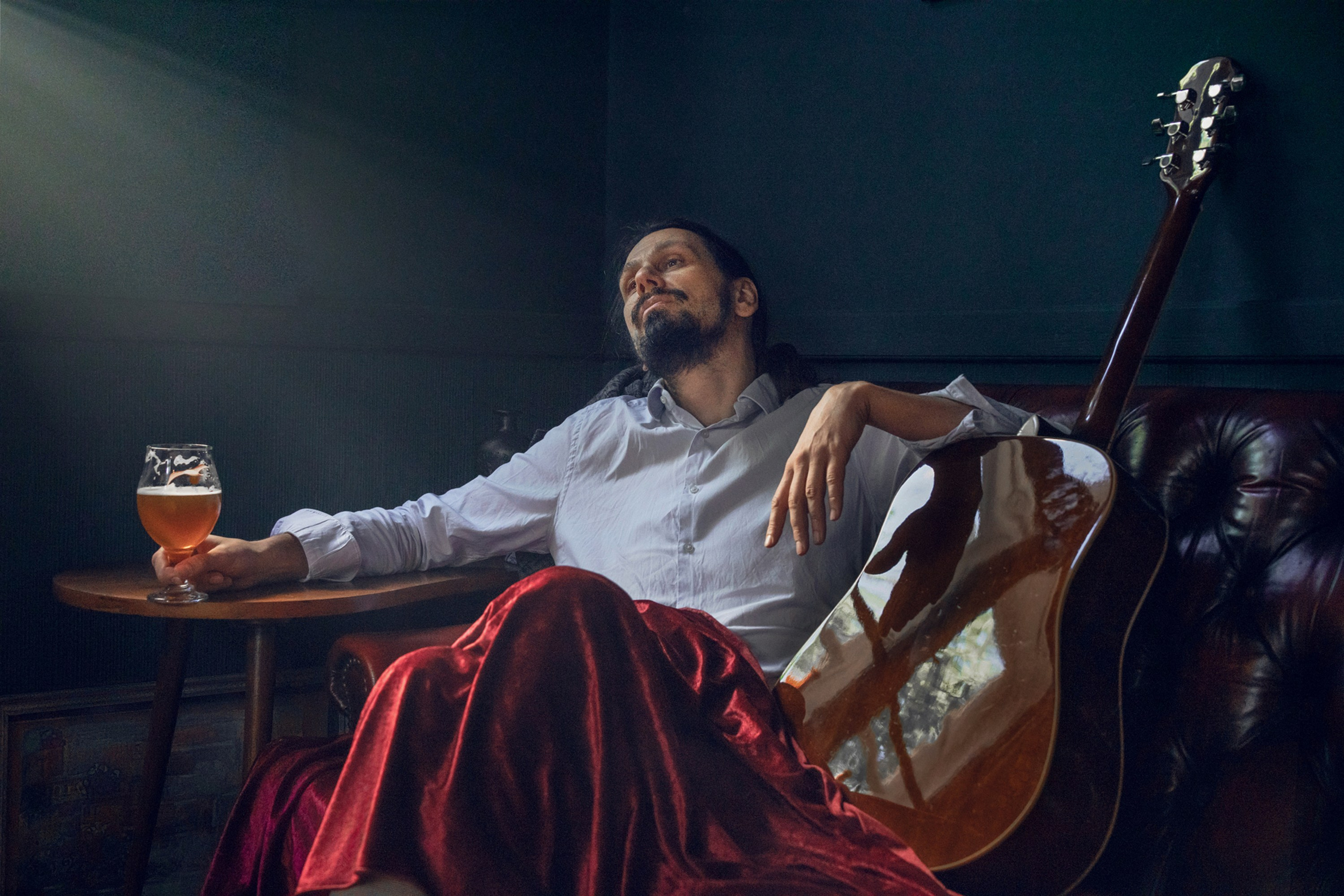 Low-key portrait of a man iwith guitar seated in a dark interior