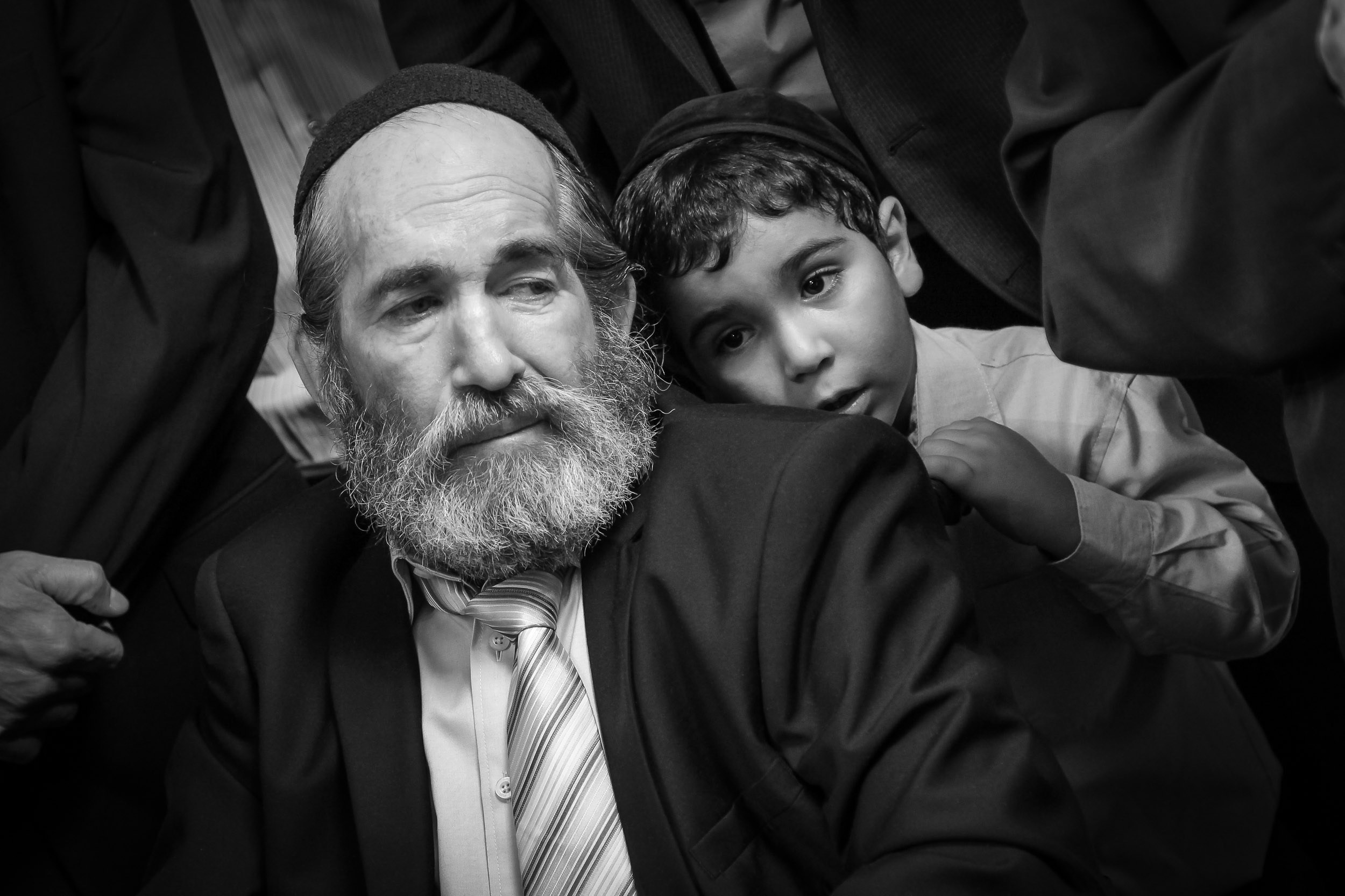An older man and a young boy wearing kippahs sit together during a wedding celebration